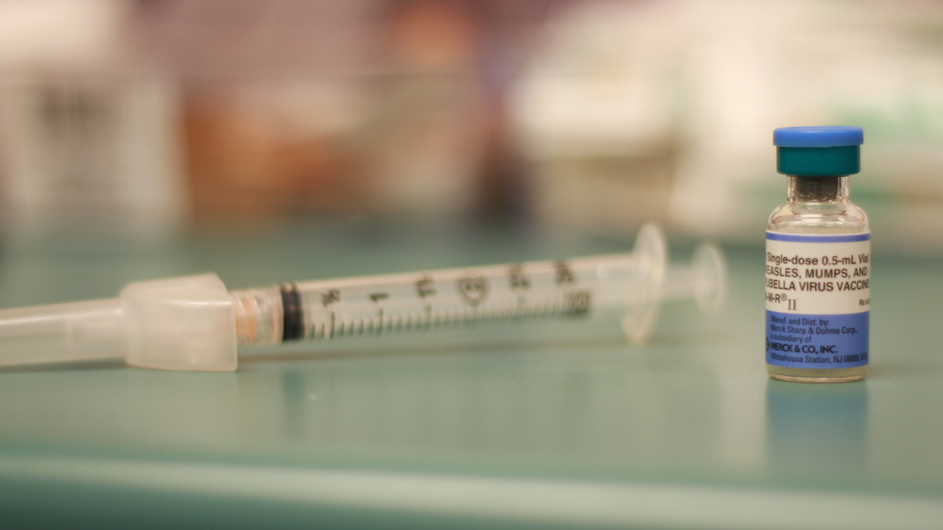 A close-up photograph of an MMR (measles, mumps and rubella) vaccine vial with a syringe in background. (Credit: Wes Little/CNN)