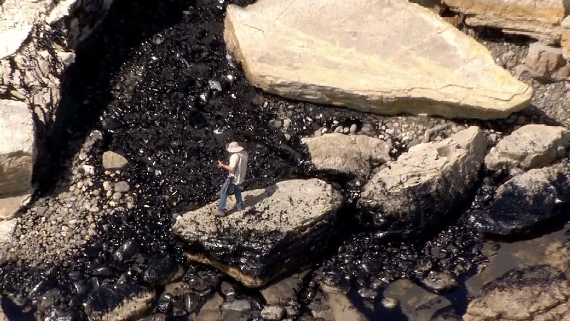 A photographer stands amid oil-slicked rocks at Refugio State Beach on May 19, 2015. (Credit: KTLA)