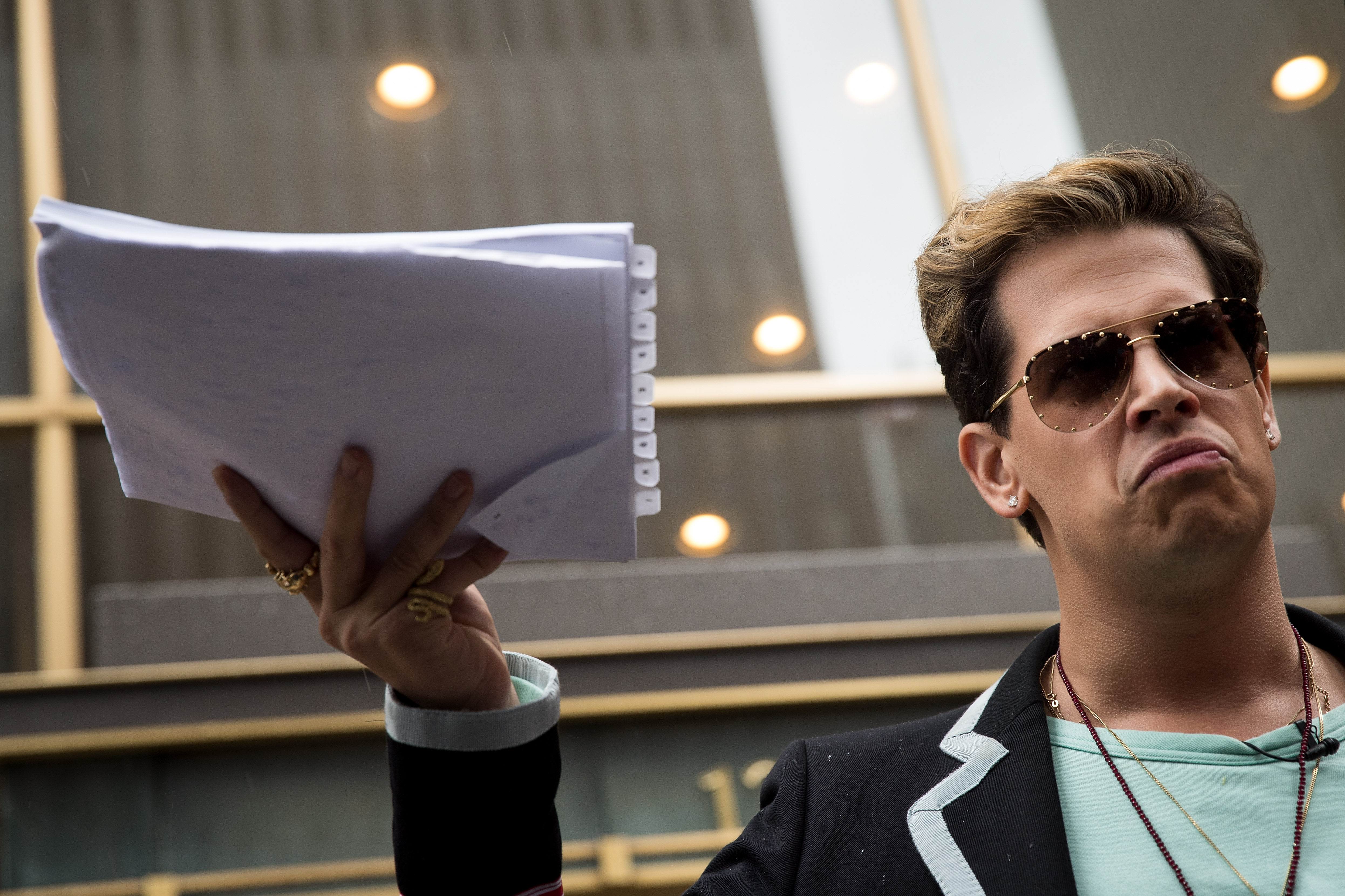 Milo Yiannopoulos holds up a copy of a legal complaint as he speaks outside the offices of Simon & Schuster publishing company, July 7, 2017, in New York City. (Credit: Drew Angerer / Getty Images)