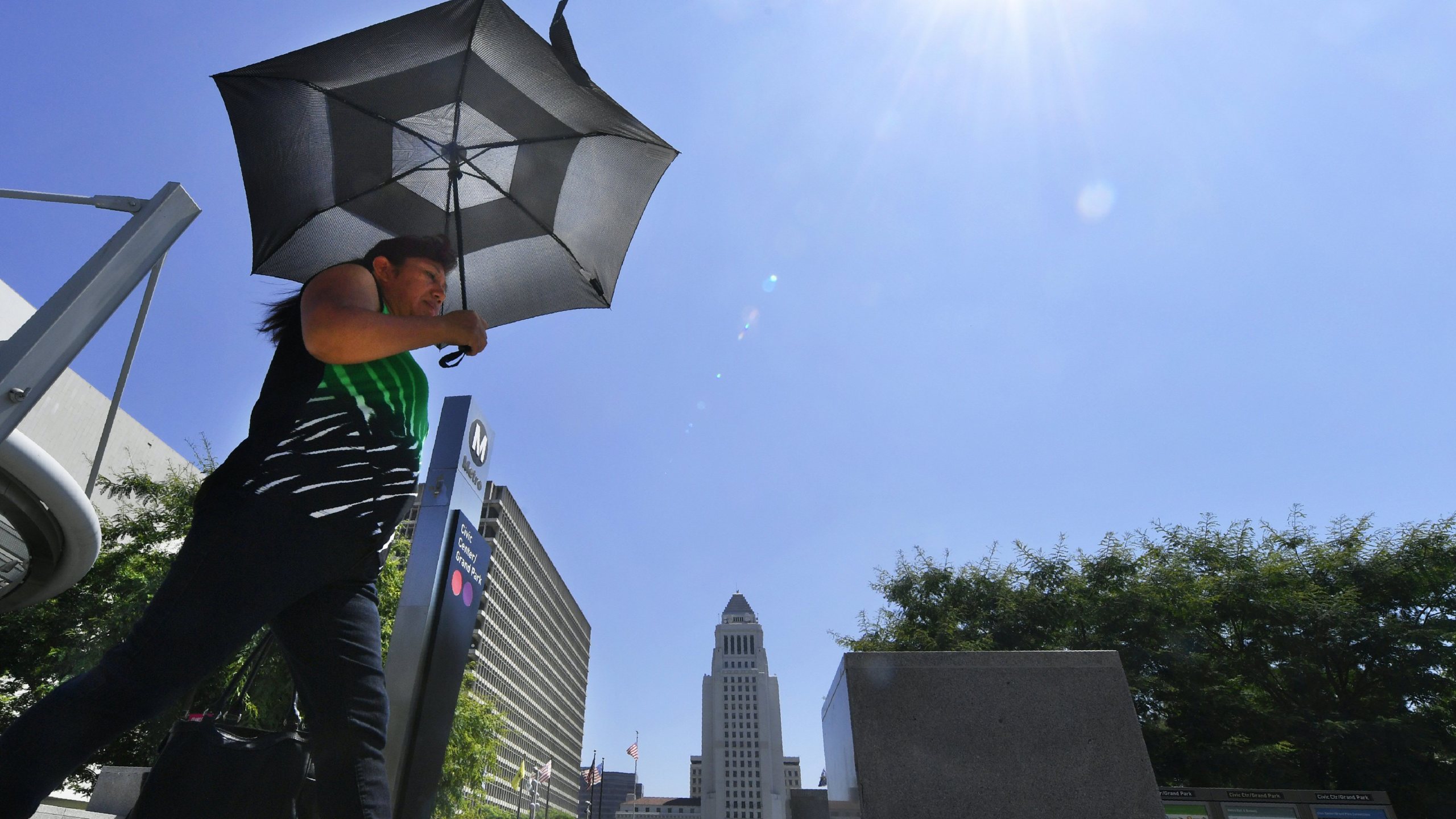 A pedestrian uses an umbrella while walking past City Hall in Los Angeles during an August, 2017 heatwave. (Credit: Frederic J. Brown/AFP/Getty Images)