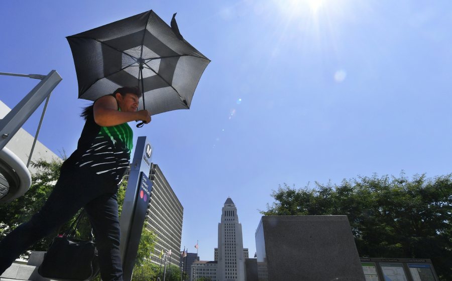 A pedestrian uses an umbrella while walking past City Hall in Los Angeles during an August, 2017 heatwave. (Credit: Frederic J. Brown/AFP/Getty Images)