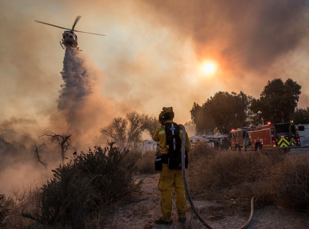 A helicopter drops water to support firefighters battling flames near a youth baseball complex outside Castaic in a photo released Dec. 9, 2017. (Credit: William G. Hartenstein / Los Angeles County Fire Dept.)