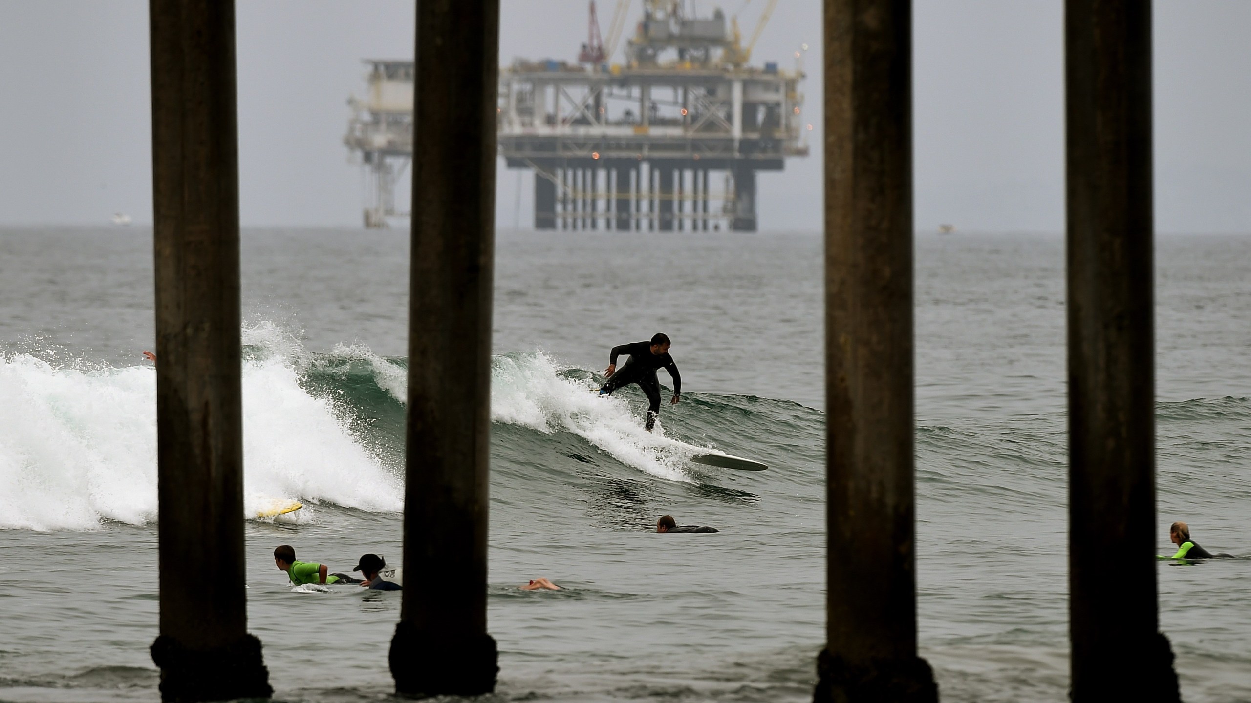 Surfers ride waves in front of an oil rig off Huntington Beach on July 31, 2015. (Credit: Mark Ralston / AFP / Getty Images)