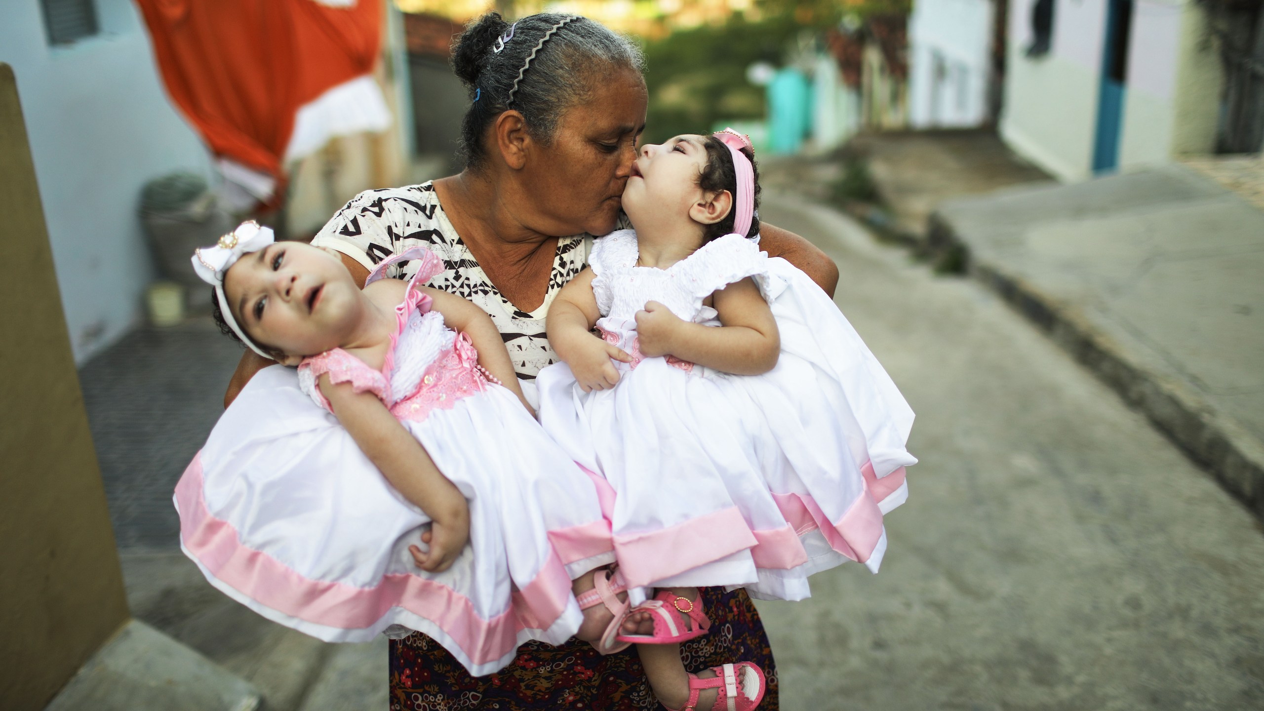 Grandmother Maria Jose holds her twin granddaughters Heloisa and Heloa Barbosa — both born with microcephaly after their mother contracted the Zika virus during pregnancy — outside of their house as they pose for photos at the twins' 1-year birthday party on April 16, 2017, in Areia, Brazil. (Credit: Mario Tama / Getty Images)