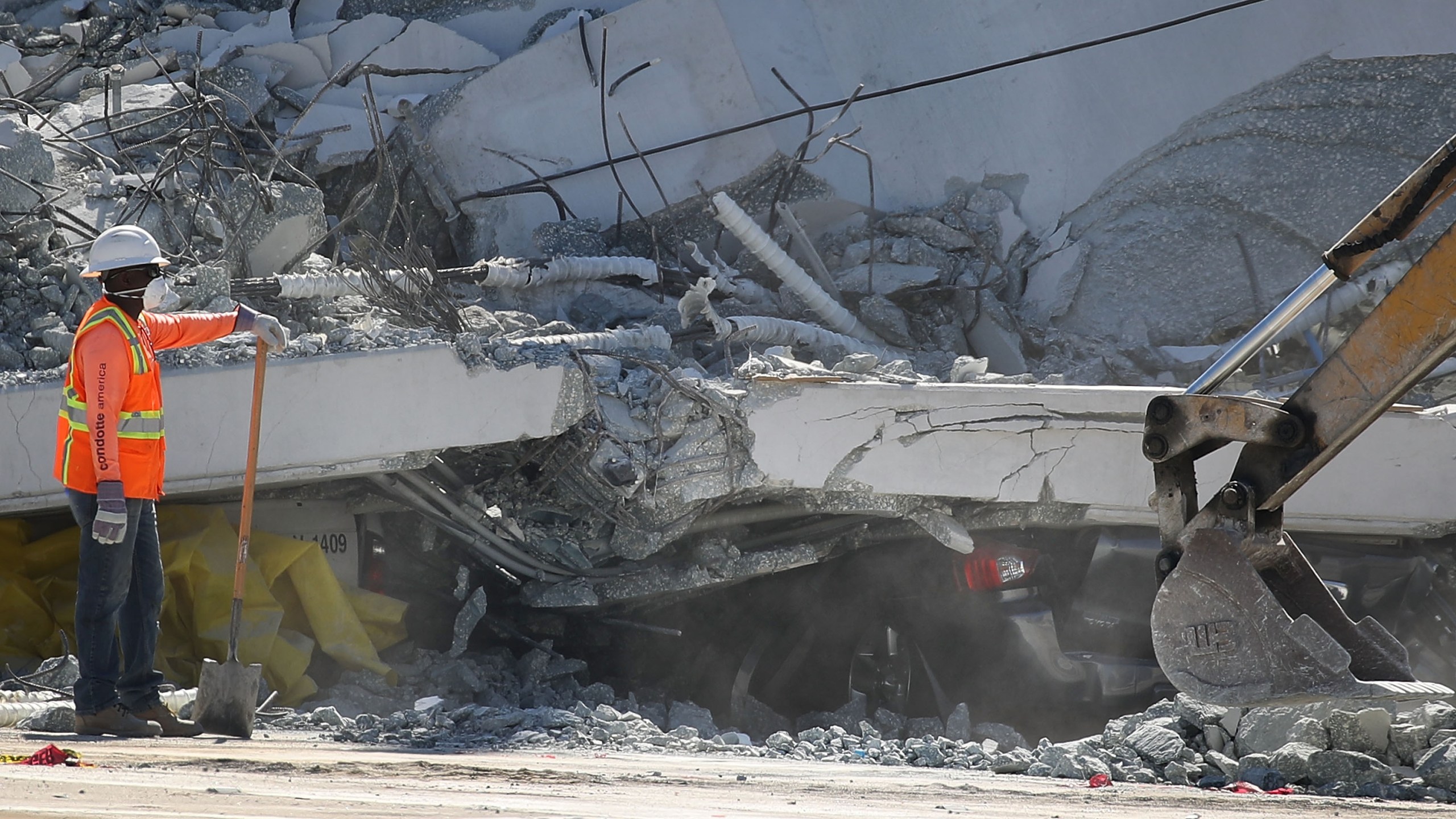 A crushed vehicle is seen near a worker as authorities investigate the scene where a pedestrian bridge collapsed a few days after it was built near Florida International University in Miami, March 16, 2018. (Credit: Joe Raedle / Getty Images)