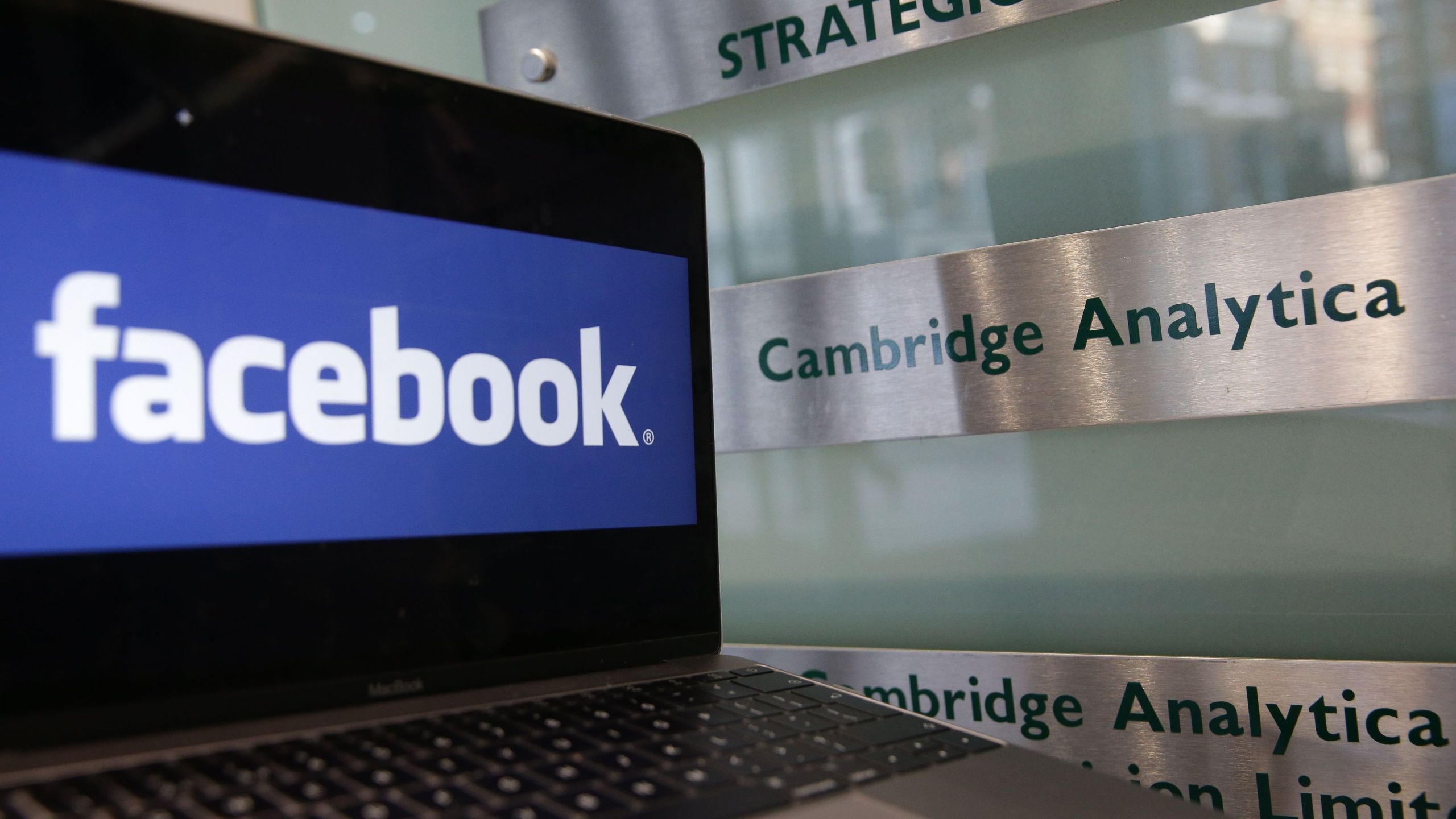 A laptop showing the Facebook logo is held alongside a Cambridge Analytica sign at the entrance to the building housing the offices of Cambridge Analytica in central London on March 21, 2018. (Credit: Daniel Leal-Olivas / AFP / Getty Images)