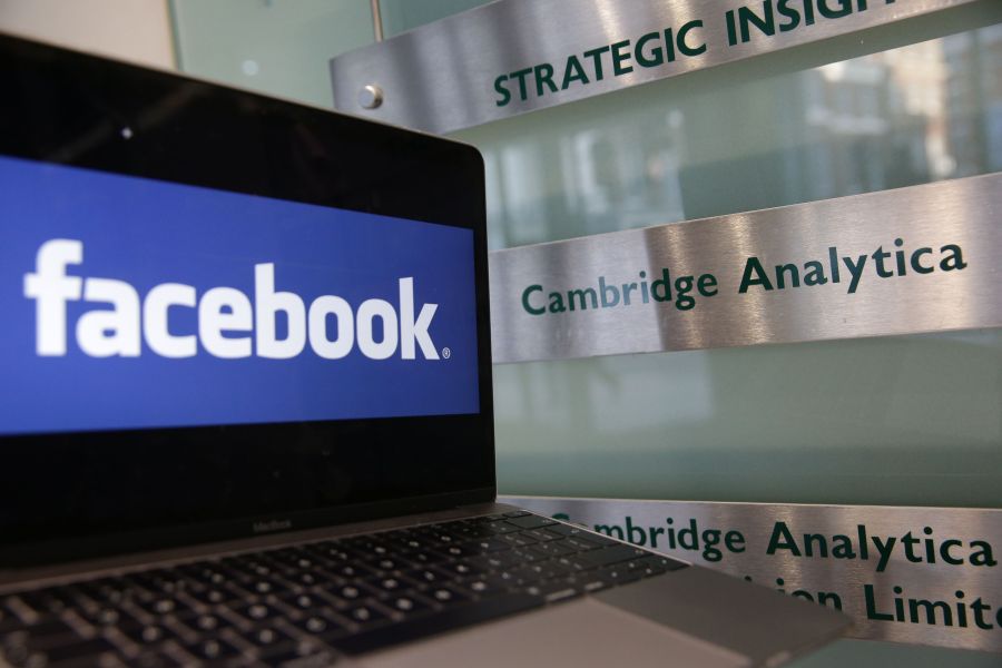 A laptop showing the Facebook logo is held alongside a Cambridge Analytica sign at the entrance to the building housing the offices of Cambridge Analytica in central London on March 21, 2018. (Credit: Daniel Leal-Olivas / AFP / Getty Images)