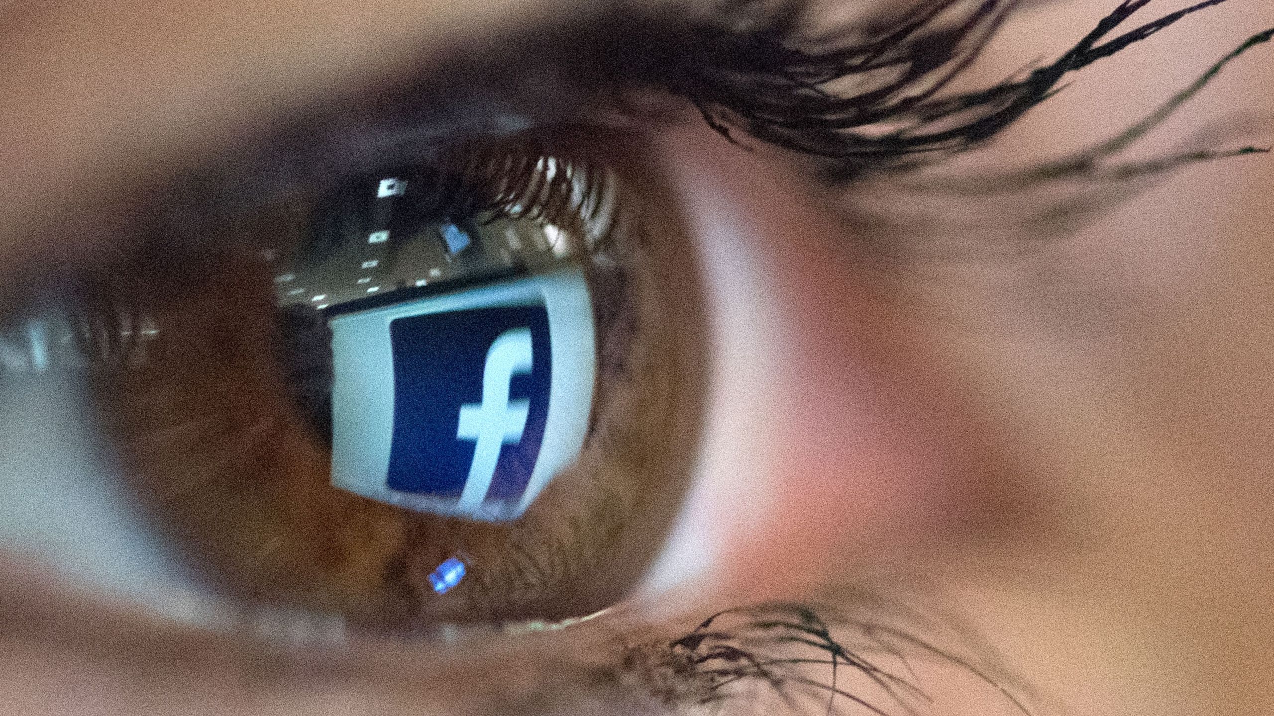 An illustration picture taken on March 22, 2018, in Paris shows a close-up of the Facebook logo in the eye of an AFP staff member posing while she looks at a flipped logo of Facebook. (Credit: Christophe Simon / AFP / Getty Images)