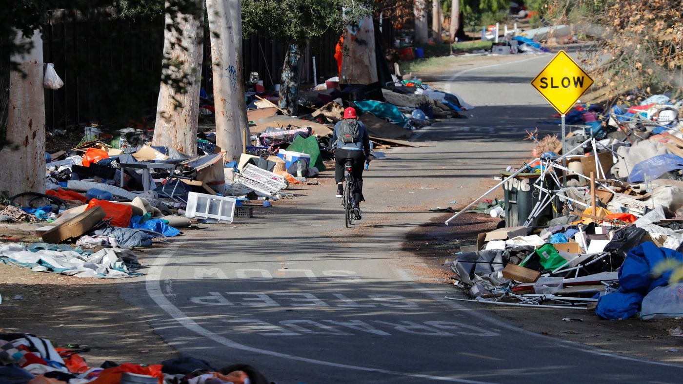 A bicyclist rides past piles of trash from the Santa Ana River homeless camp after it was cleared and more than 700 people relocated in Anaheim in February. (Credit: Allen J. Schaben / Los Angeles Times)