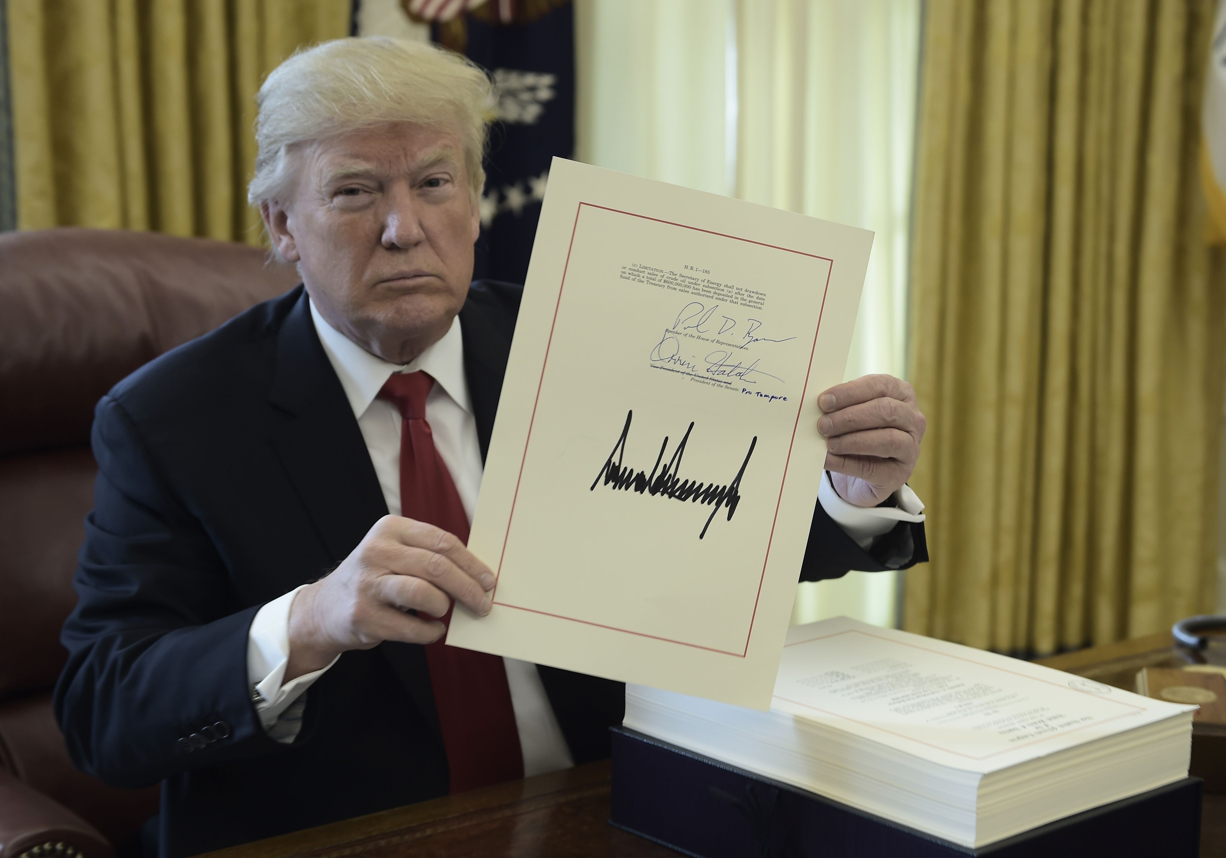 President Trump holds up a copy of the tax reform bill he signed in the Oval Office on Dec. 22, 2017. (Credit: Brendan Smialowski / AFP / Getty Images)