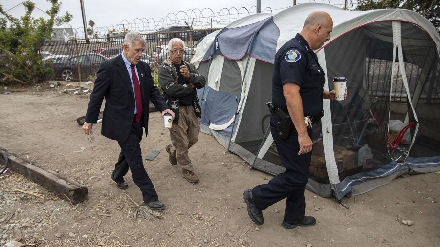 U.S. District Judge David Carter, left, homeless activist Lou Noble and Deputy Chief Ken Gominsky of the Santa Ana Police Department walk past a tent along railroad tracks near Main Street in Santa Ana on June 5, 2018. (Credit: Scott Smeltzer / Daily Pilot)