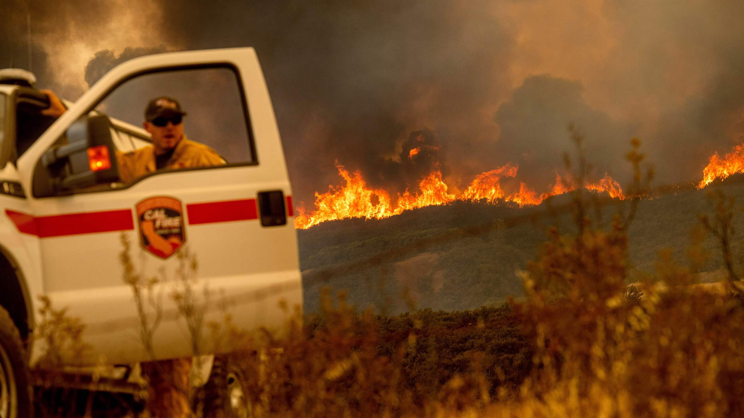 The Ranch Fire, part of the Mendocino Complex Fire, crests a ridge as Cal Fire Battalion Chief Matt Sully directs firefighting operations near Clearlake Oaks on Aug. 5, 2018. (Credit: Noah Berger / AFP / Getty Images)