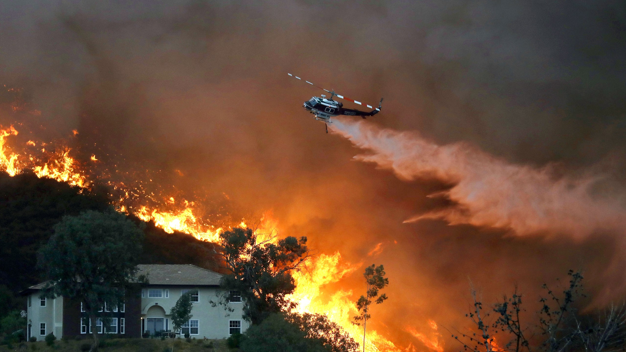 A firefighting helicopter makes a water drop as the Holy Fire burns near homes in Lake Elsinore on Aug. 9, 2018. (Credit: Mario Tama / Getty Images)