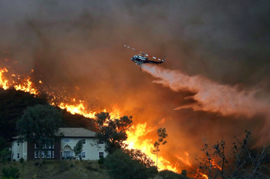 A firefighting helicopter makes a water drop as the Holy Fire burns near homes in Lake Elsinore on Aug. 9, 2018. (Credit: Mario Tama / Getty Images)