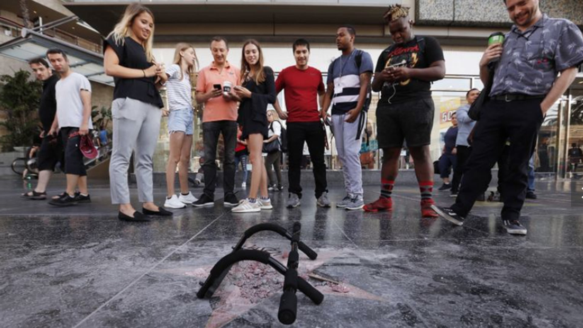 People standing on the streets of Hollywood look down at a heavily damaged star honoring Donald Trump after it was vandalized in August 2018. (Credit: Al Seib / Los Angeles Times)