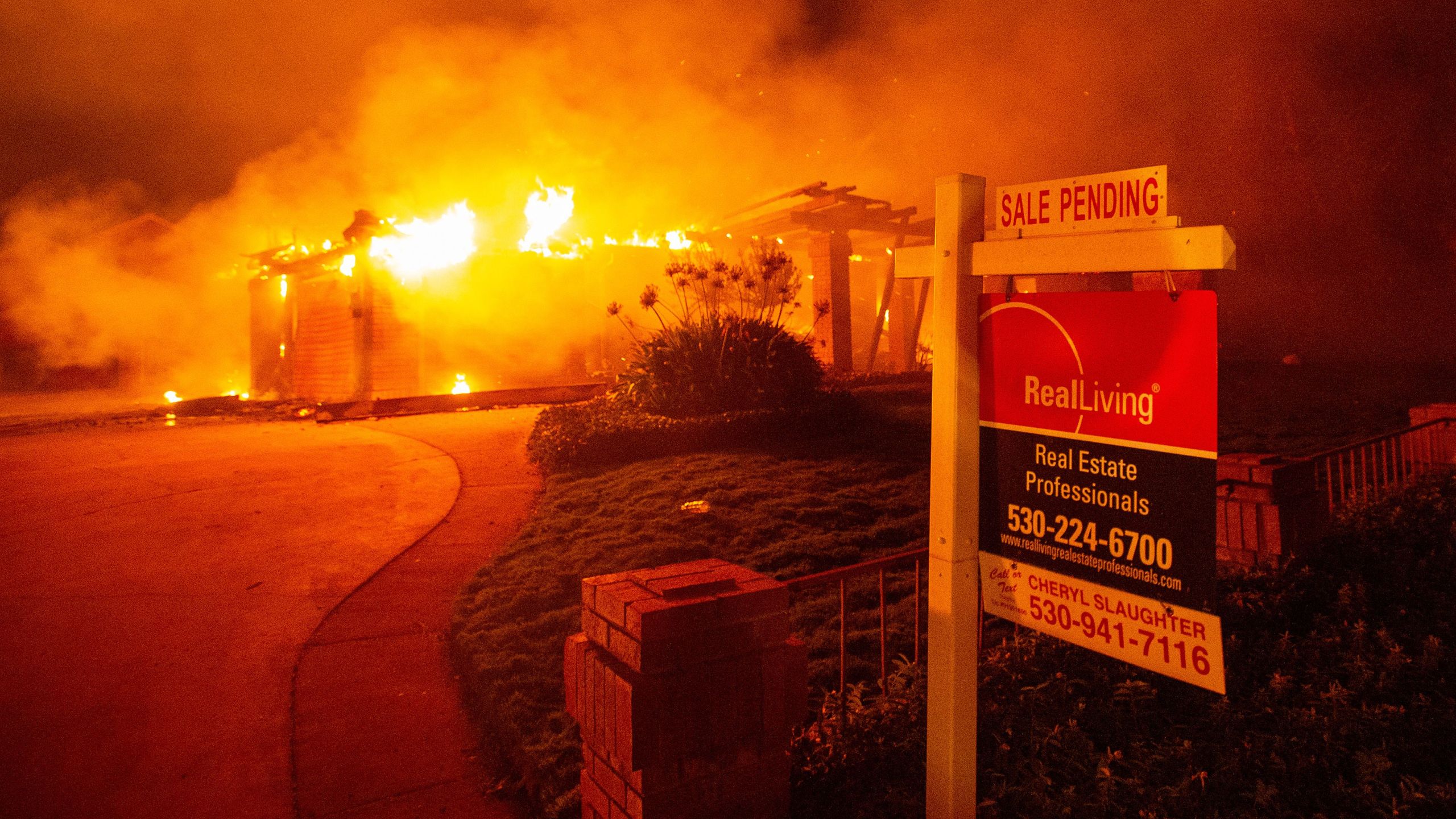 A real estate sign is seen in front of a burning home in Redding during the Carr Fire on July 27, 2018. (Credit: Josh Edelson / AFP / Getty Images)