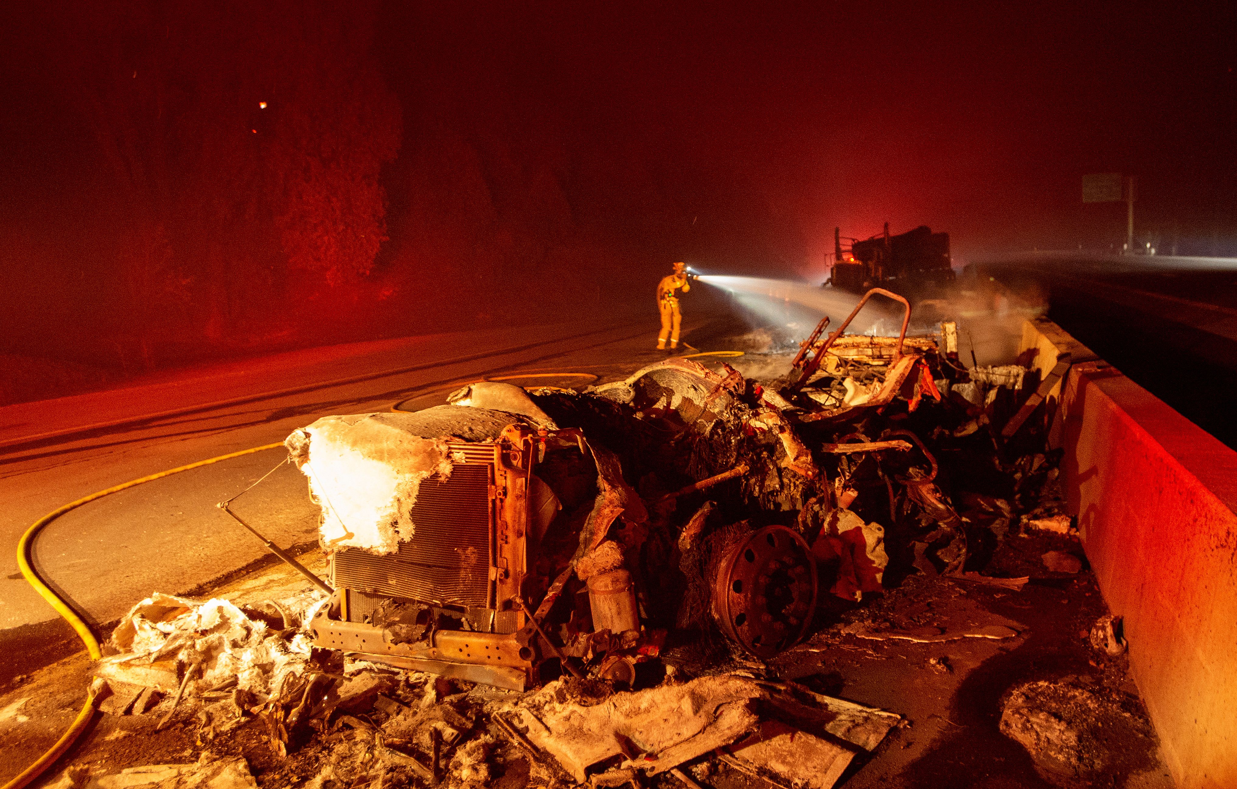 A firefighter sprays down a burned big rig truck that was abandoned along Interstate 5 as the Delta Fire tore through the region in Delta on Sept. 5, 2018. (JOSH EDELSON/AFP/Getty Images)