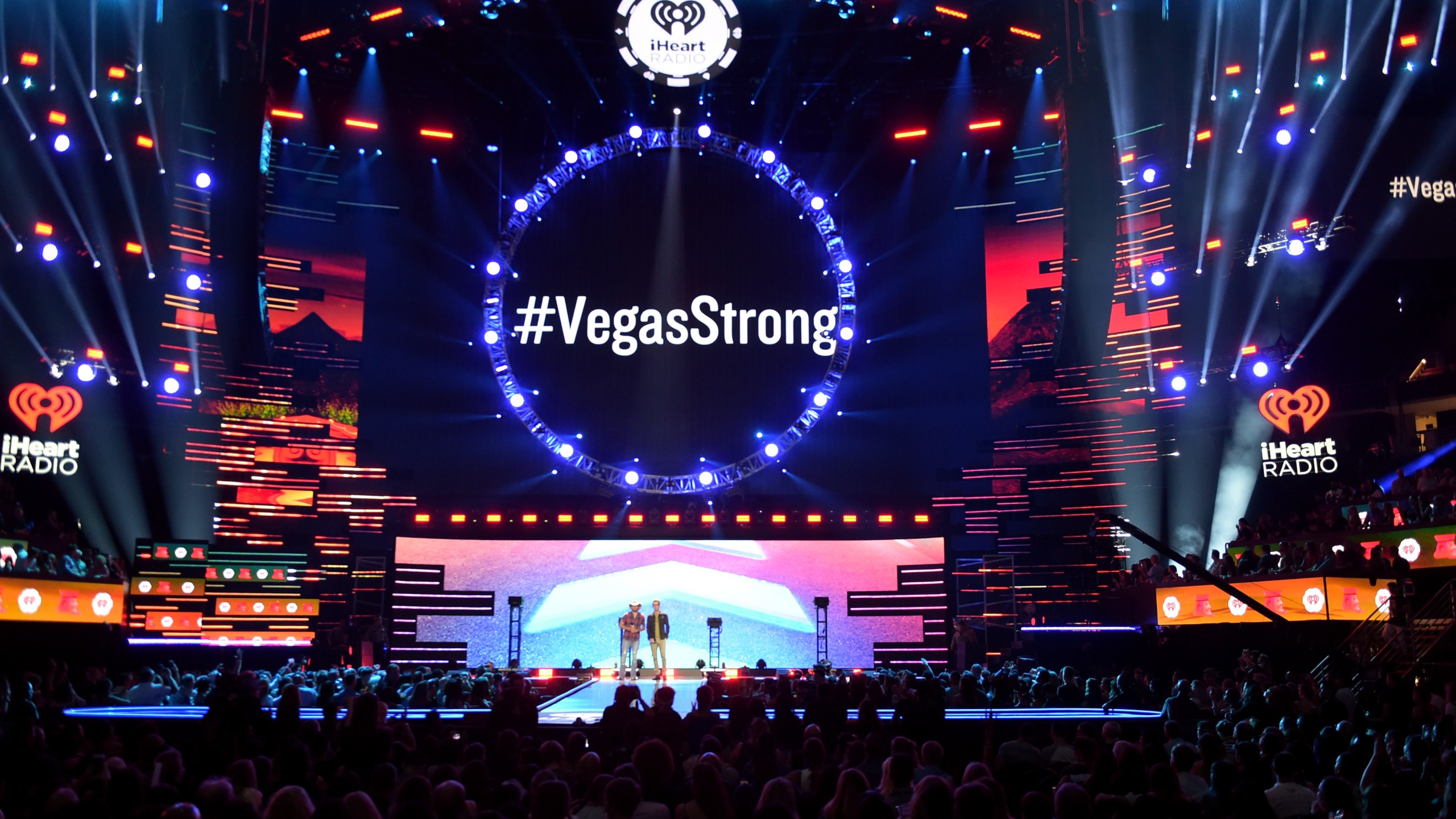 '#VegasStrong' is projected on a video screen while Jason Aldean (L) and Bobby Bones speak onstage during the 2018 iHeartRadio Music Festival at T-Mobile Arena on September 21, 2018 in Las Vegas, Nevada. (Credit: Kevin Winter/Getty Images for iHeartMedia)