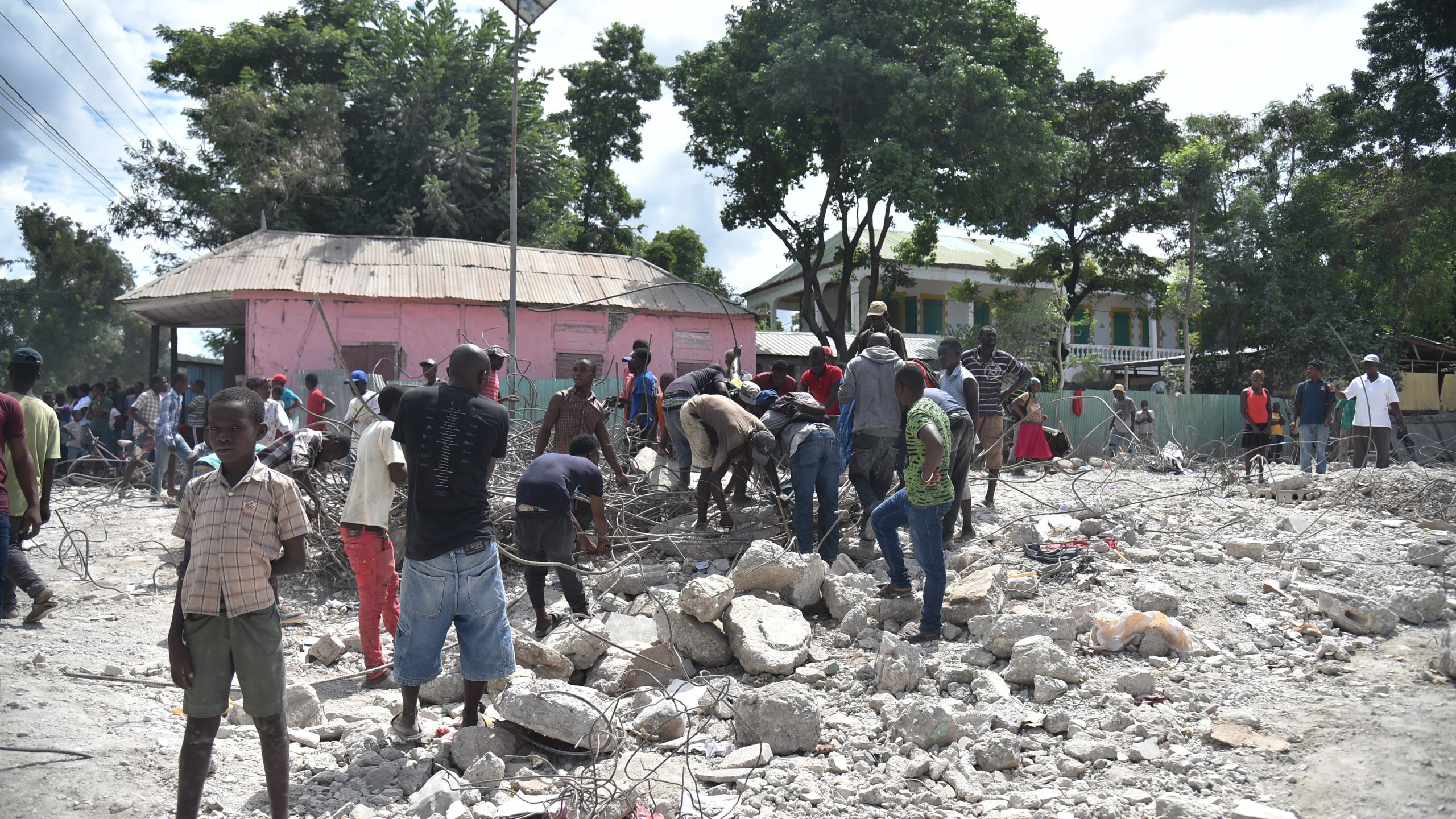 Haitian people collect metal on Oct. 7, 2018 in Gros Morne, Haiti from a destroyed auditorium after an earthquake struck north of Haiti on Oct. 6, 2018. (Credit: HECTOR RETAMAL/AFP/Getty Images)