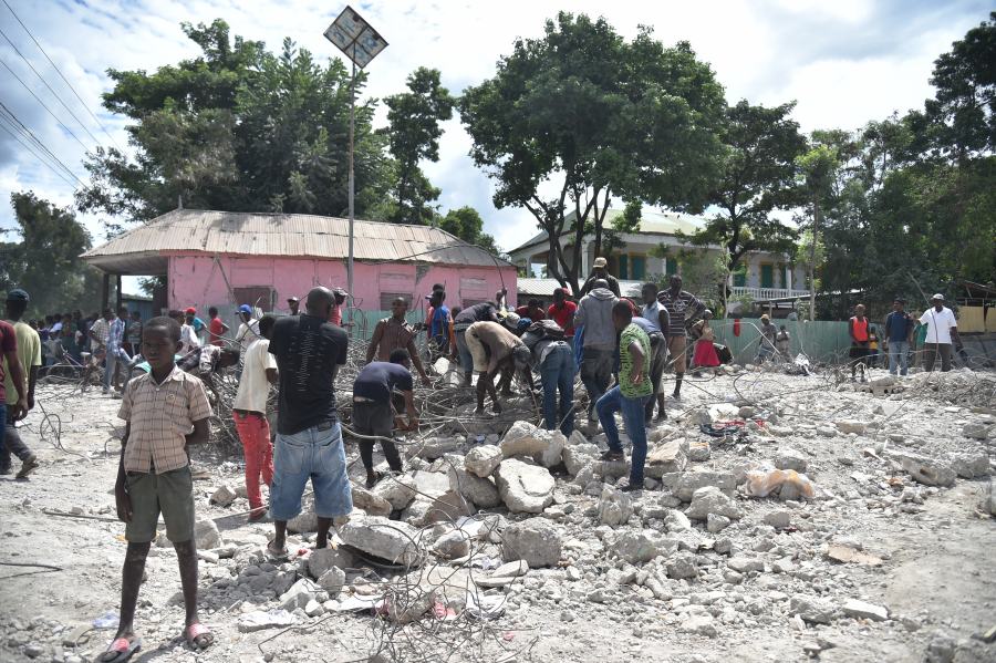 Haitian people collect metal on Oct. 7, 2018 in Gros Morne, Haiti from a destroyed auditorium after an earthquake struck north of Haiti on Oct. 6, 2018. (Credit: HECTOR RETAMAL/AFP/Getty Images)