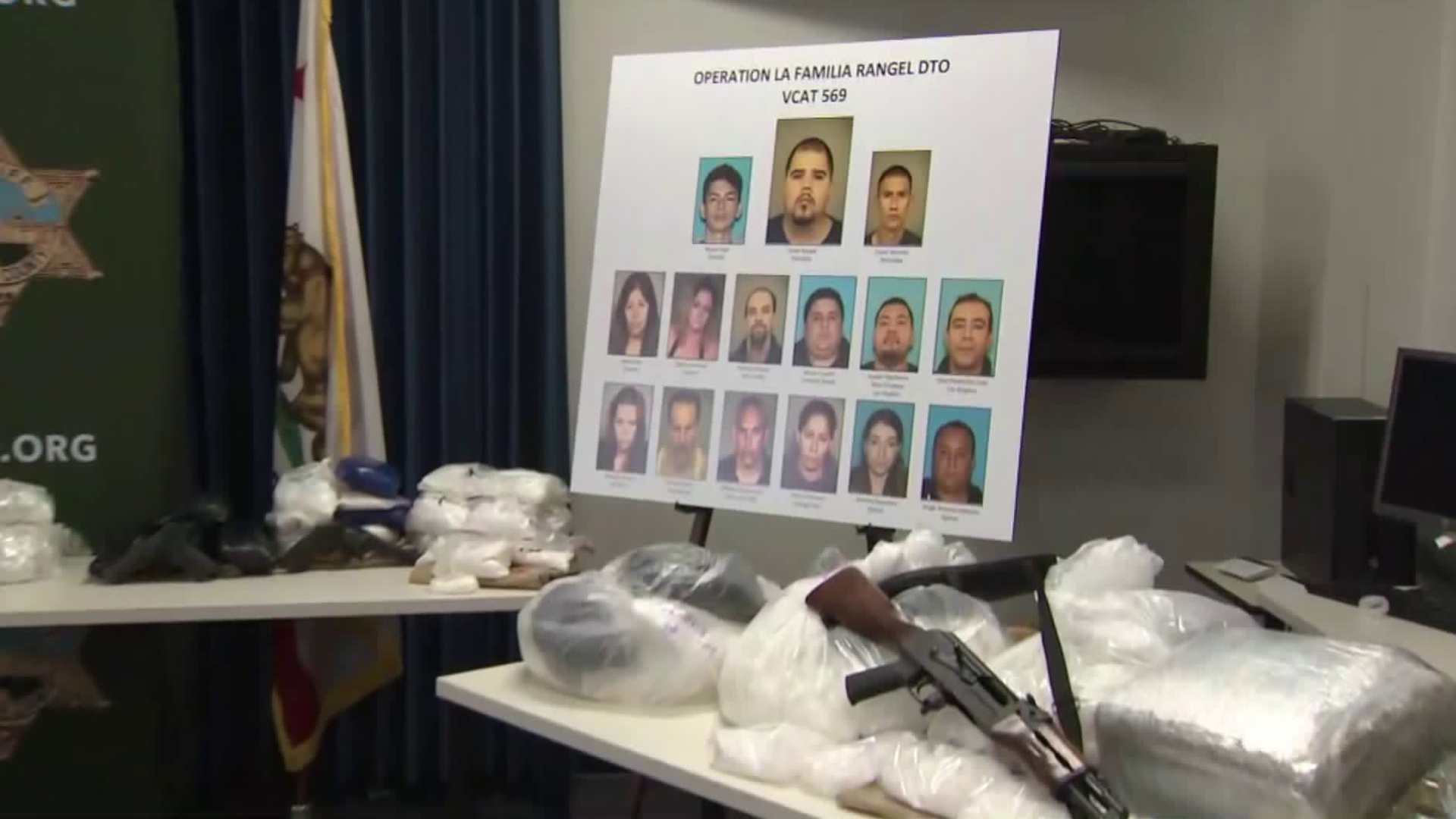 Thirteen people arrested who were linked to the Sinaloa Cartel are shown in photos surrounded by drugs and guns seized during the investigation on Oct. 9, 2018. (Credit: KTLA)