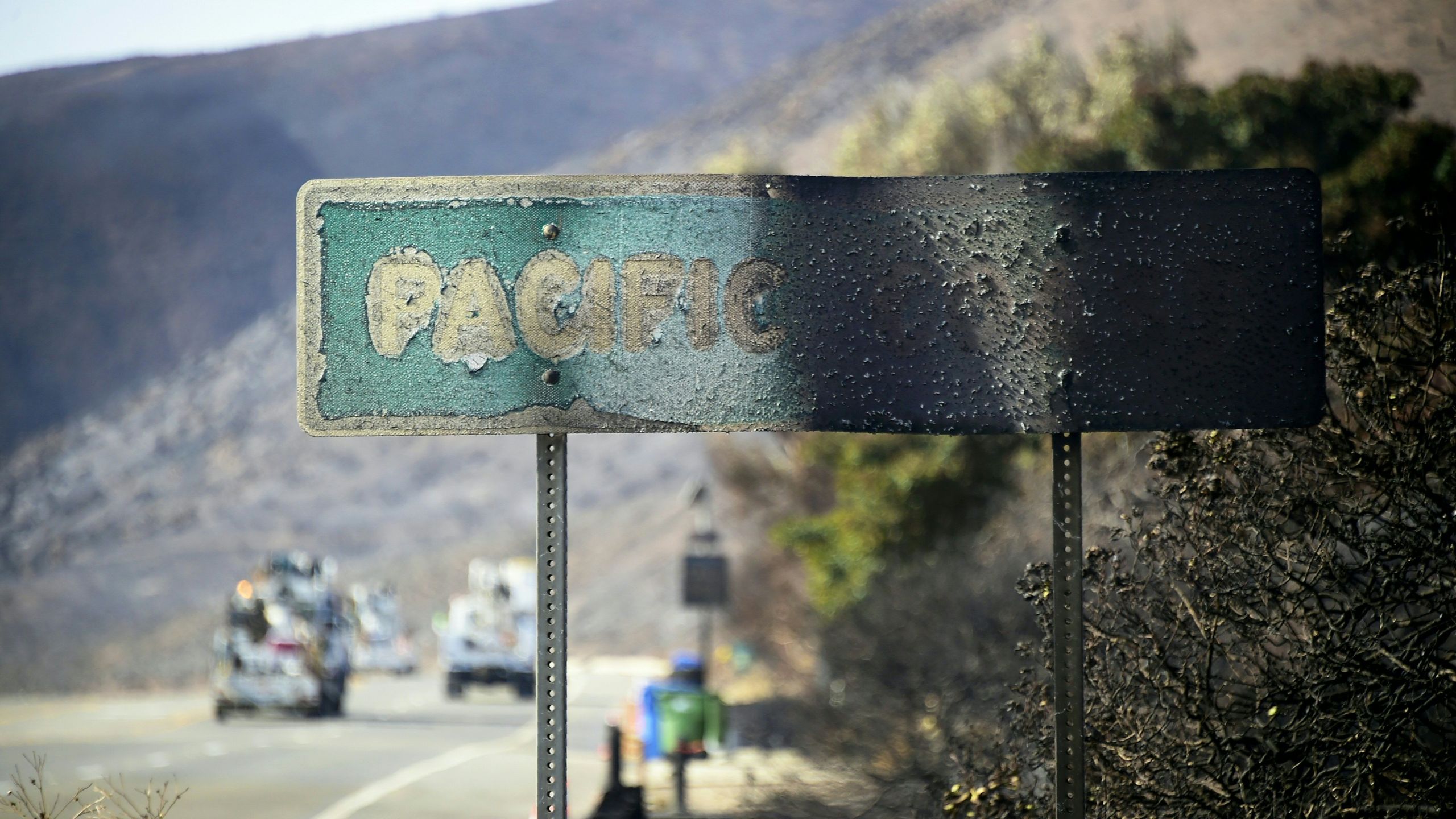 A fire-damaged Pacific Coast sign remains standing along the Pacific Coast Highway amid the blackened and charred hills from the Woolsey Fire in Malibu on Nov. 15, 2018. (Credit: Frederic J. Brown / AFP / Getty Images)