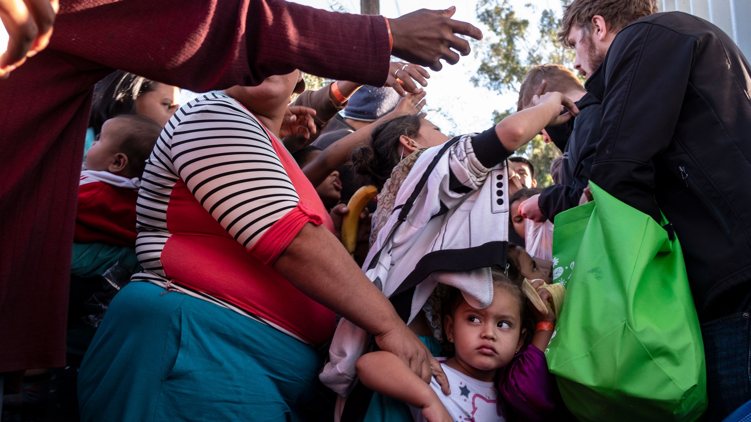 A group of Central American migrants — mostly from Honduras — wanting to reach the United States struggle for fruit given by volunteers outside a temporary shelter in Tijuana, near the U.S.-Mexico border fence, on Nov. 23, 2018. (Credit: Guillermo Arias / AFP / Getty Images)