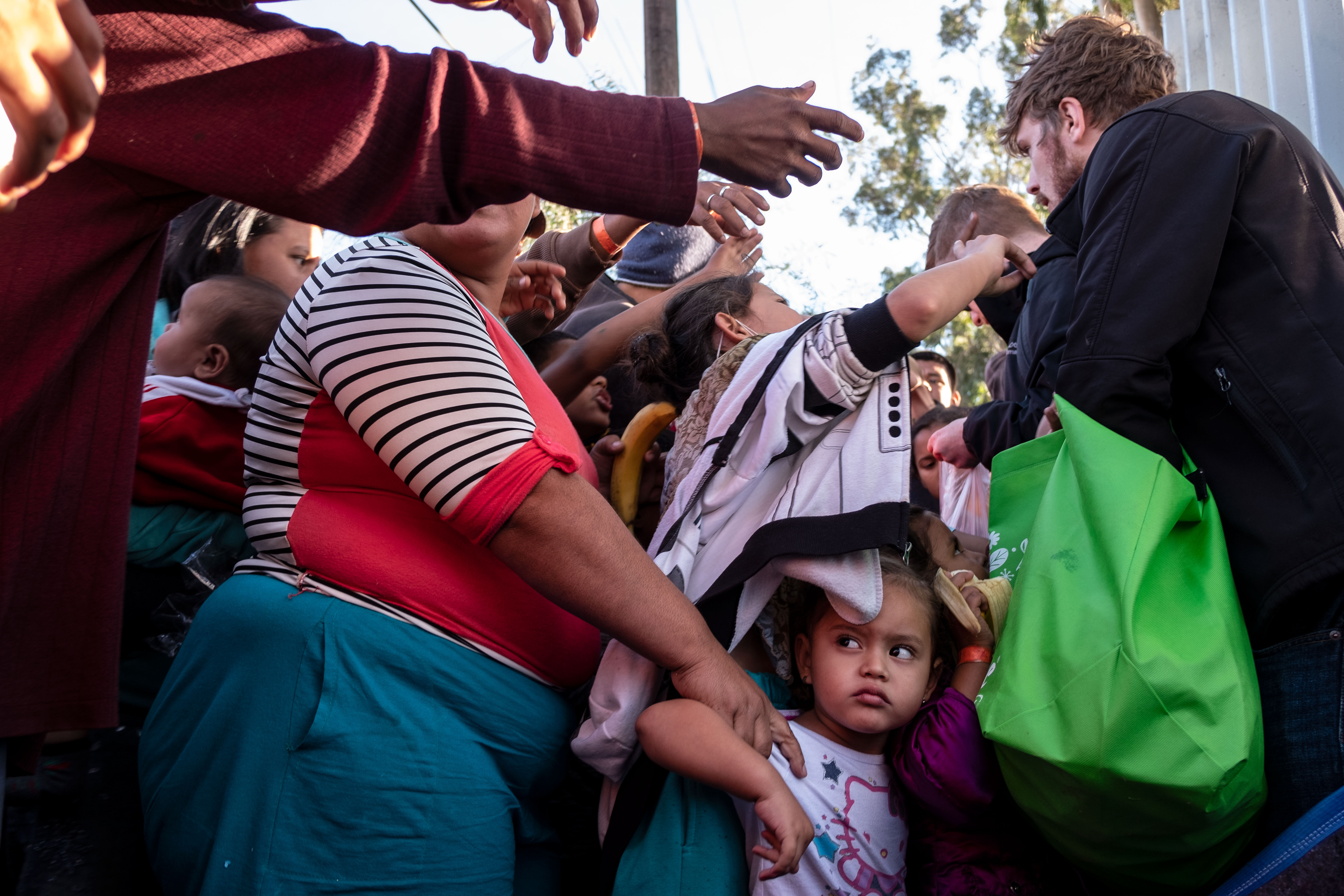 A group of Central American migrants — mostly from Honduras — wanting to reach the United States struggle for fruit given by volunteers outside a temporary shelter in Tijuana, near the U.S.-Mexico border fence, on Nov. 23, 2018. (Credit: Guillermo Arias / AFP / Getty Images)