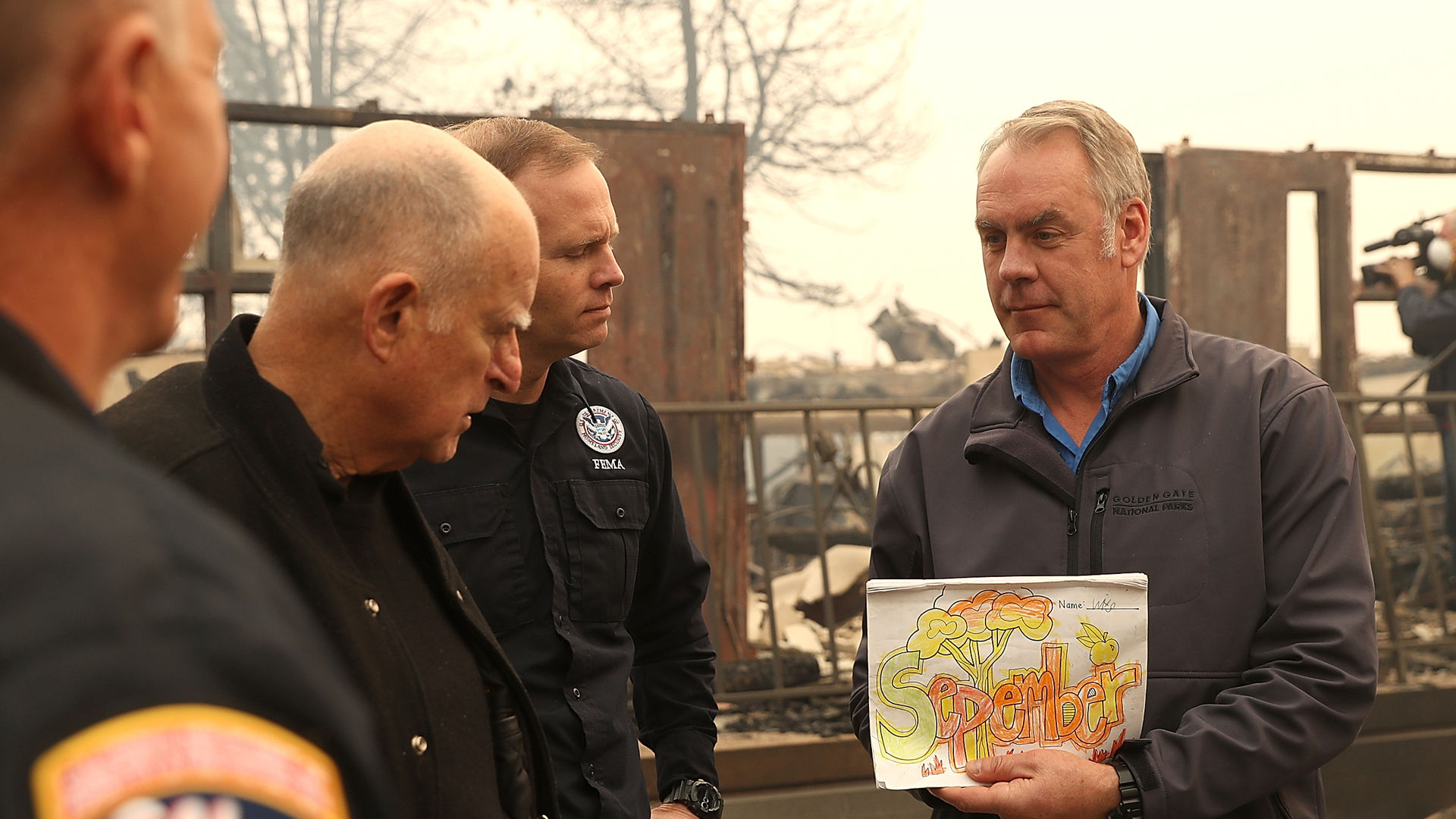 Gov. Jerry Brown and FEMA Administrator Brock Long look on as U.S. Secretary of the Interior Ryan Zinke holds up a child's school work as they tour a school burned by the Camp Fire on Nov. 14, 2018, in Paradise. (Credit: Justin Sullivan/Getty Images)