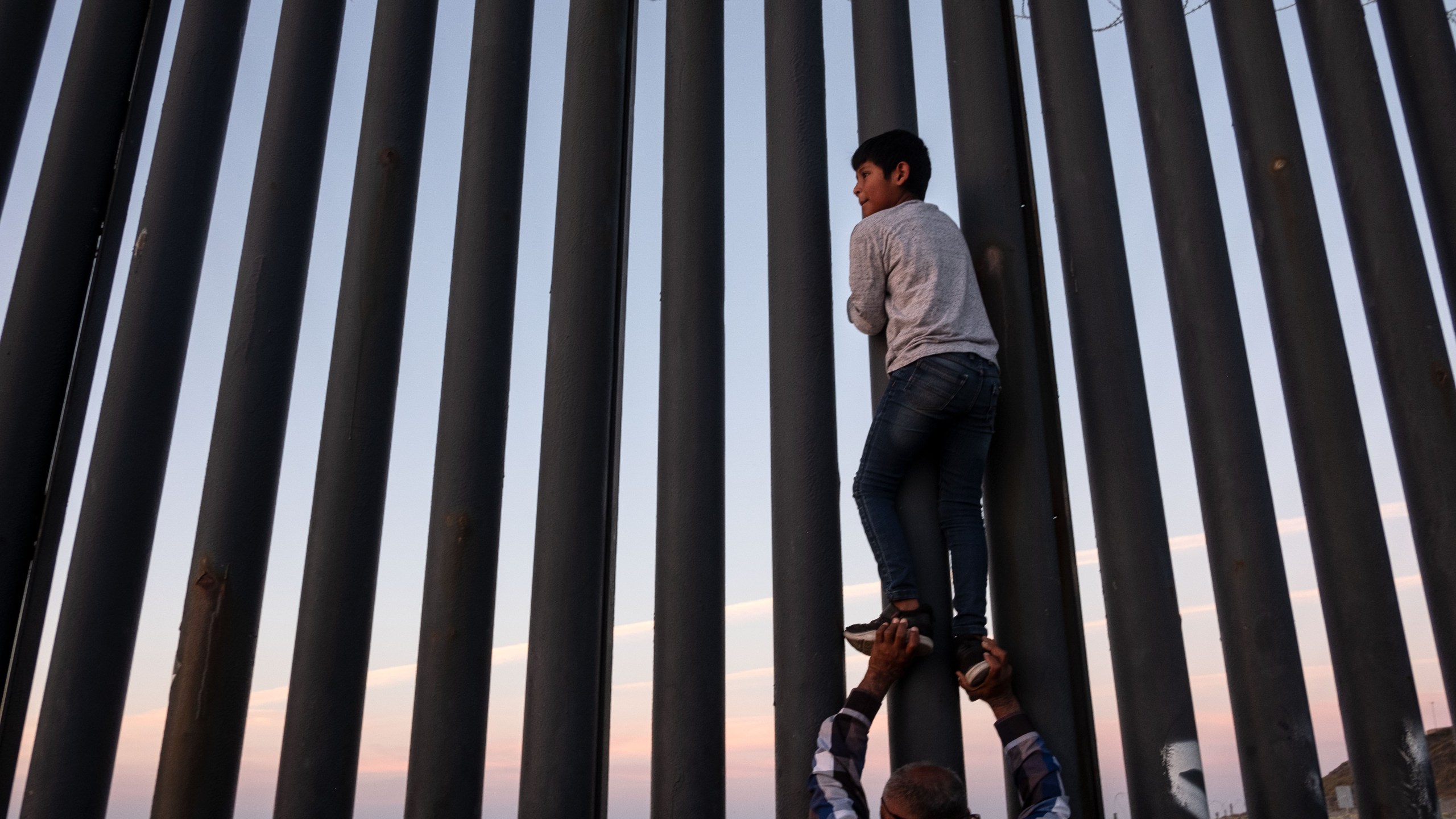 A man helps a boy to have a better look at the US-Mexico border wall in Playas de Tijuana, northwestern Mexico, November 18, 2018. (Credit: GUILLERMO ARIAS/AFP/Getty Images)