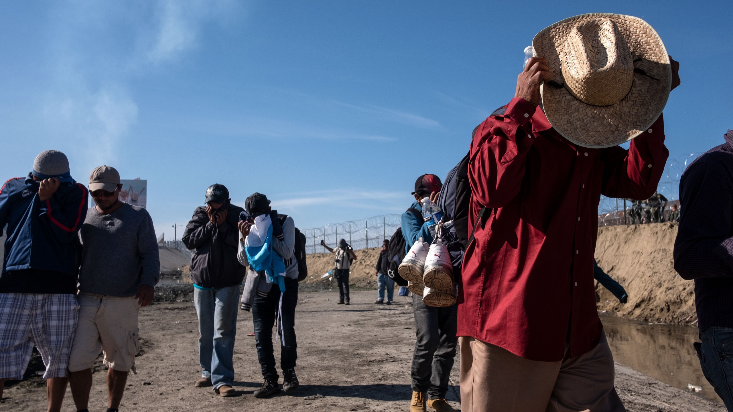 Central American migrants cover their faces next to the Tijuana River near the El Chaparral border crossing in Tijuana, Mexico, after the U.S. Border Patrol threw tear gas to disperse them after an alleged verbal dispute on Nov. 25, 2018. (Credit: Guillermo Arias / AFP / Getty Images)