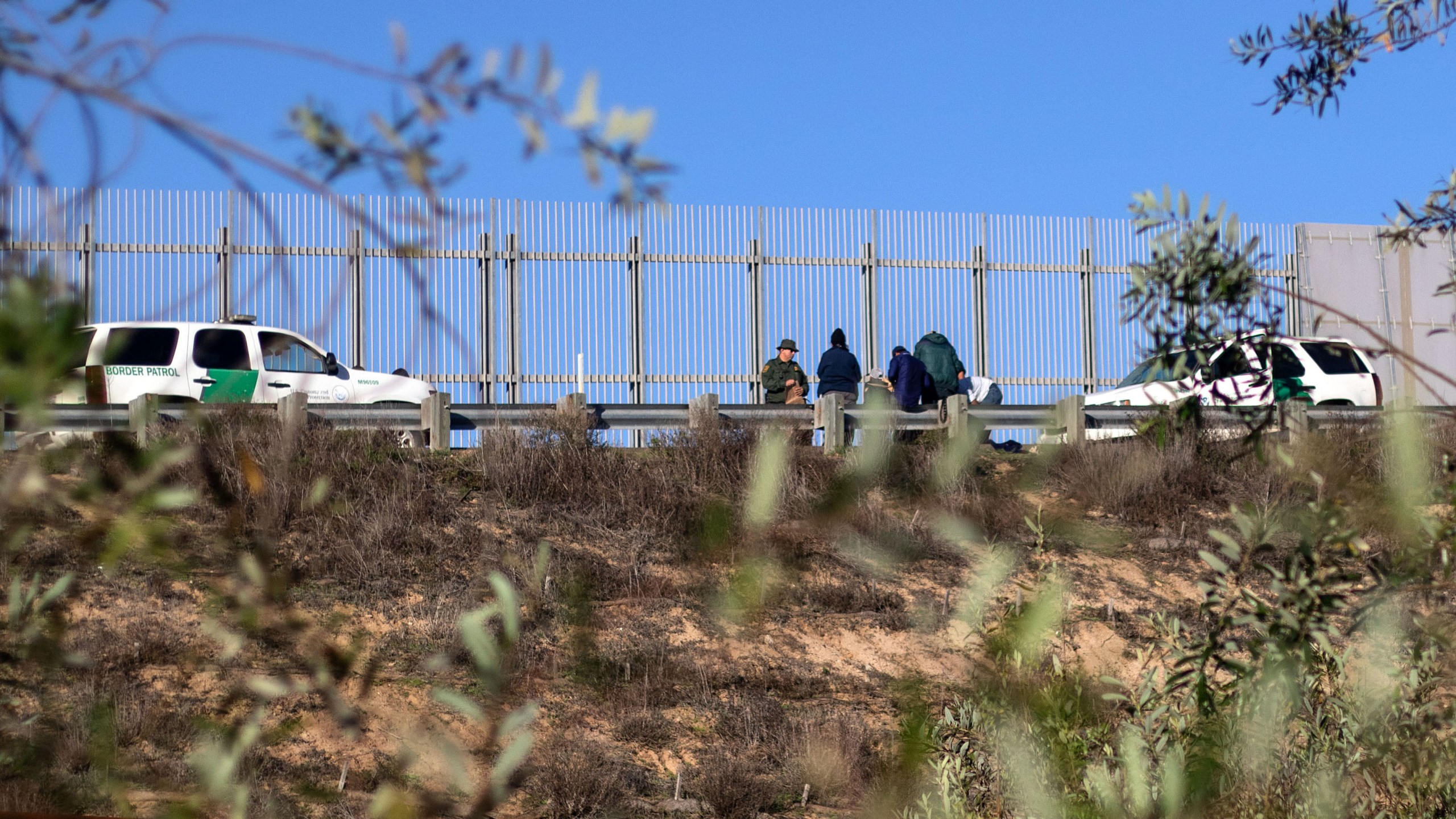 A group of migrants traveling in the Central American caravan are taken in custody by the U.S. Border Patrol after crossing the border fence into San Diego County, as seen from Playas de Tijuana, Mexico, on Dec. 12, 2018. (Credit: Guillermo Arias / AFP / Getty Images)