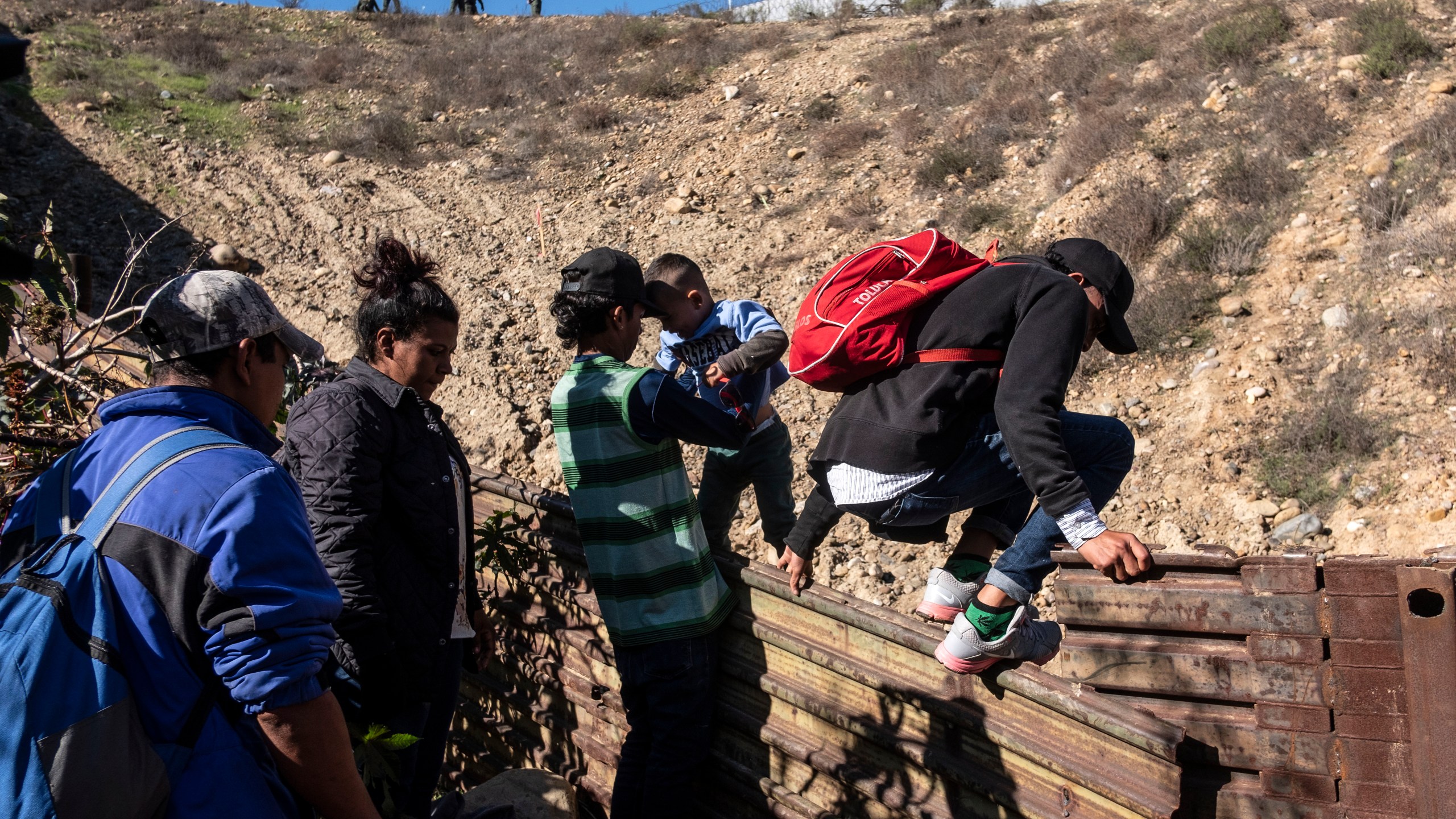 A group of Central American migrants -traveling in a caravan- cross the Mexico-US border fence to San Diego County, from Tijuana, on Dec. 16, 2018. (Credit: Guillermo Arias/AFP/Getty Images)