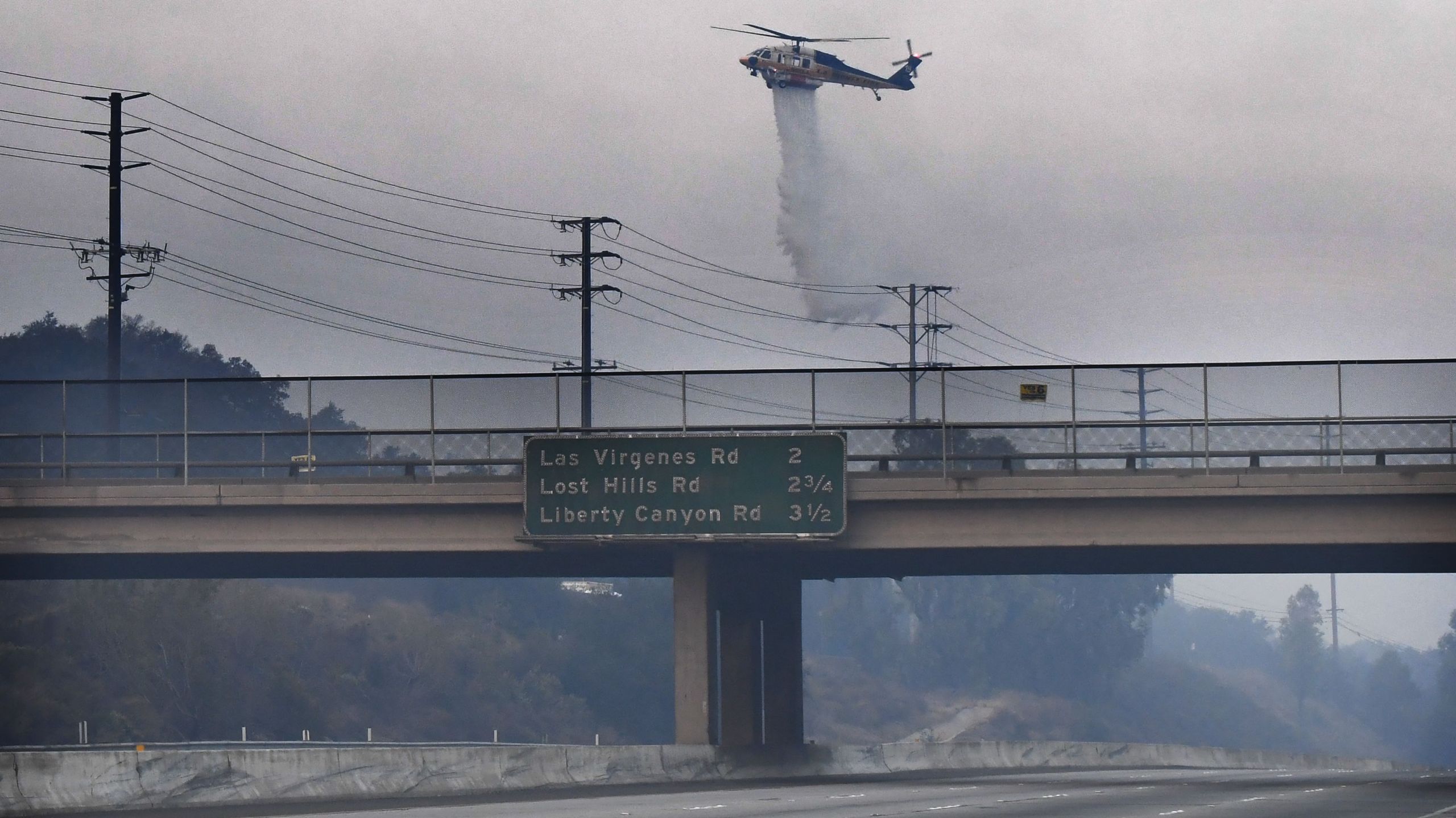 A helicopter drops water on a hot spot from the Woolsey Fire on Nov. 10, 2018 along the 101 Freeway in Calabasas. (Credit: ROBYN BECK/AFP/Getty Images)