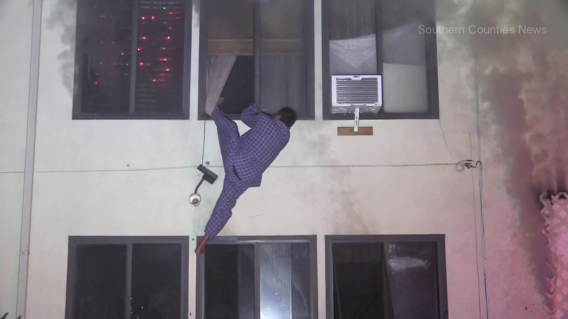 A man climbs out of a window to escape the flames of a burning apartment building in Garden Grove on Jan. 3, 2019. (Credit: Southern Counties News)