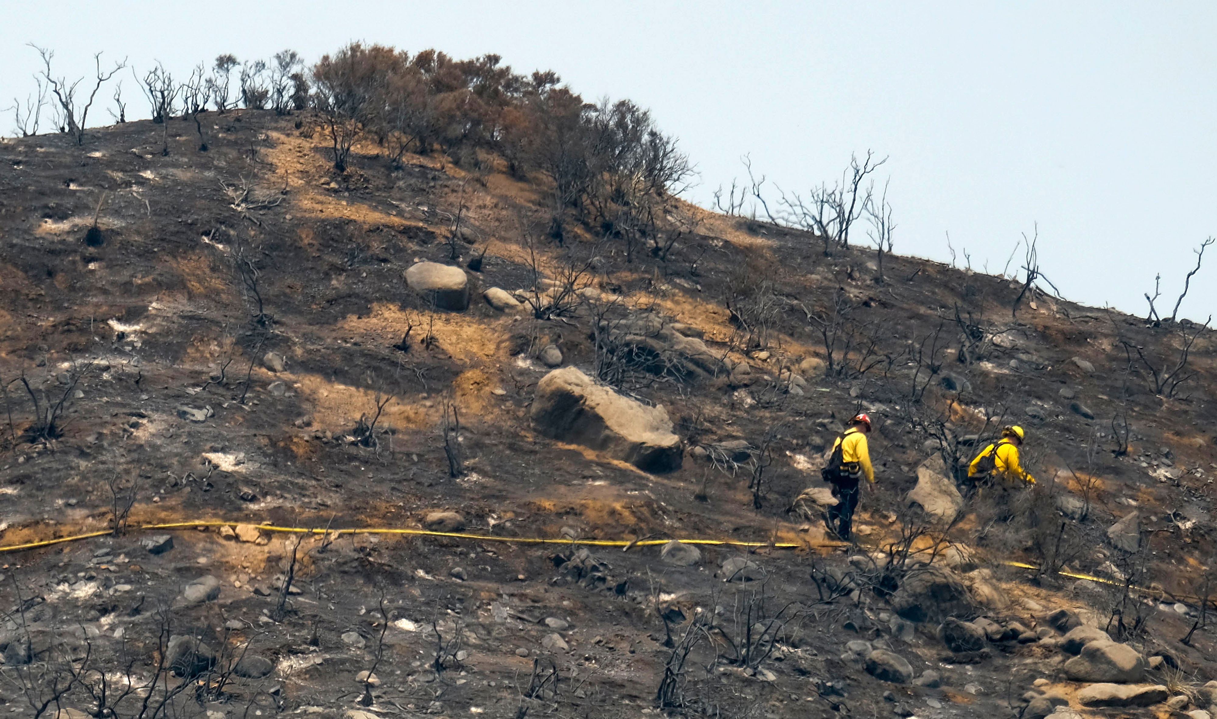 In this file photo taken on Aug. 10, 2018, firefighters walk through an area burned by the Holy Fire in Lake Elsinore. (Credit: Ringo Chiu / AFP / Getty Images)