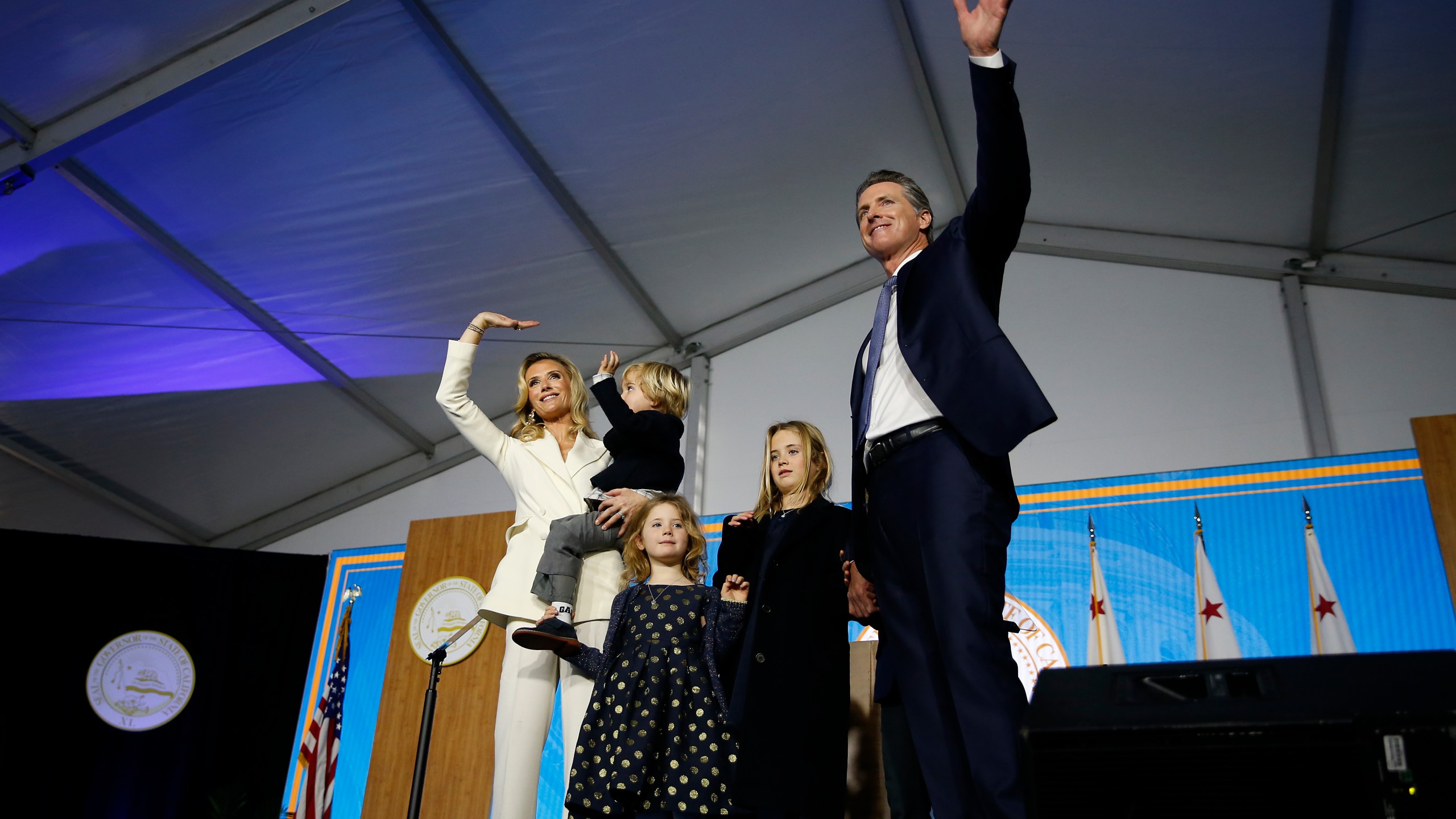 Gov. Gavin Newsom gestures to the crowd alongside his wife, Jennifer Siebel Newsom, and (from left) children Dutch, Montana and Brooklynn on Jan. 7, 2019, during his swearing in in Sacramento. (Credit: Stephen Lam / Getty Images)