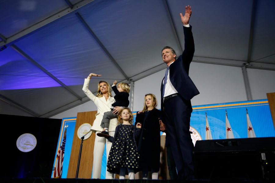 Gov. Gavin Newsom gestures to the crowd alongside his wife, Jennifer Siebel Newsom, and (from left) children Dutch, Montana and Brooklynn on Jan. 7, 2019, during his swearing in in Sacramento. (Credit: Stephen Lam / Getty Images)