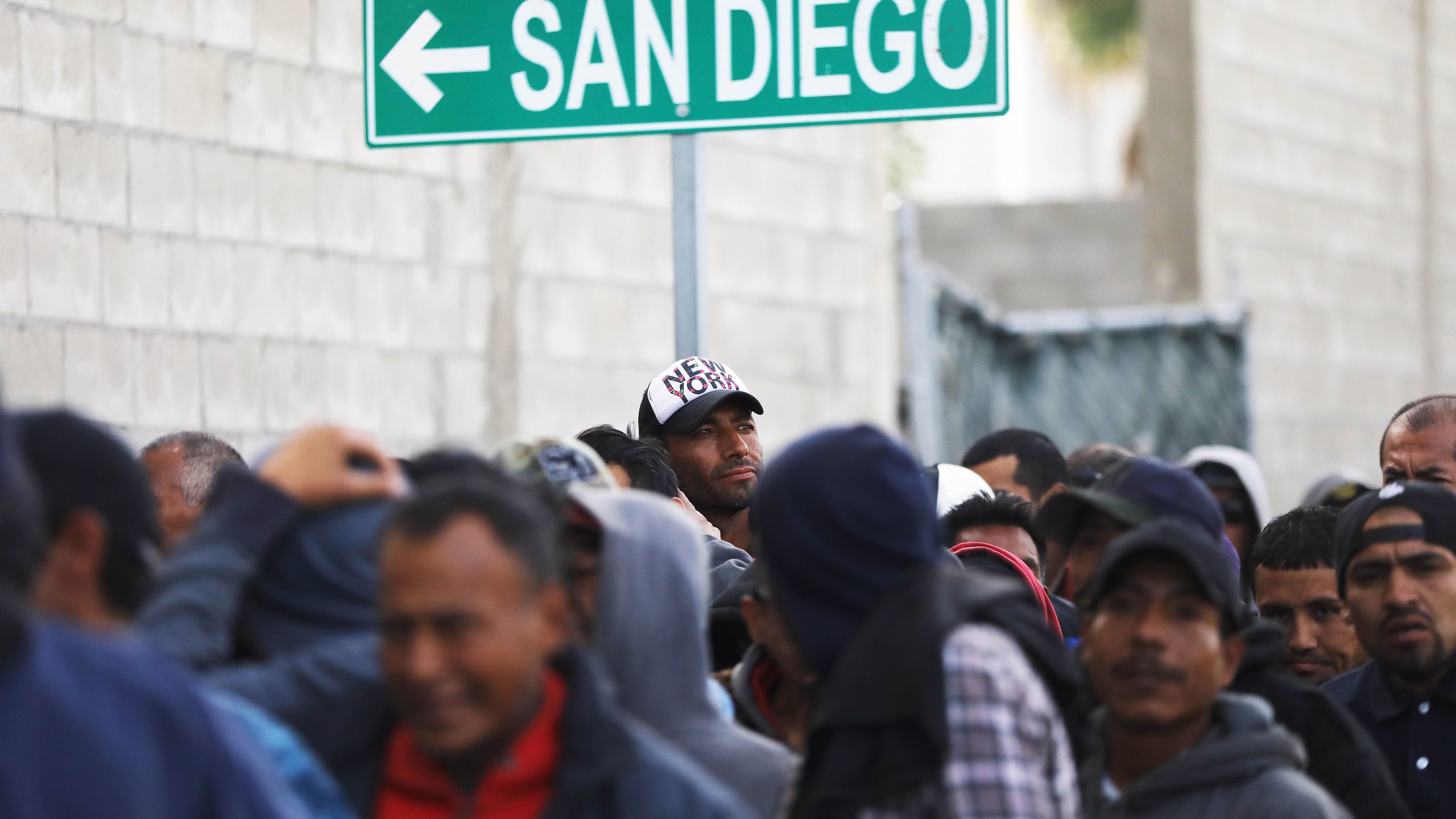 Migrants line up for free breakfast at the Desayunador Salesiano Padre Chava shelter and soup kitchen in front of sign for San Diego on March 9, 2018 in Tijuana, Mexico. (Credit: Mario Tama/Getty Images)