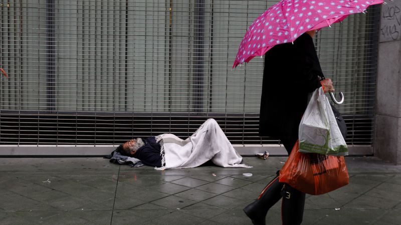 Esteban Velasquez, 54, tries to stay warm as pedestrians walk along South Broadway in downtown Los Angeles on a rainy day in January. (Credit: Francine Orr / Los Angeles Times)