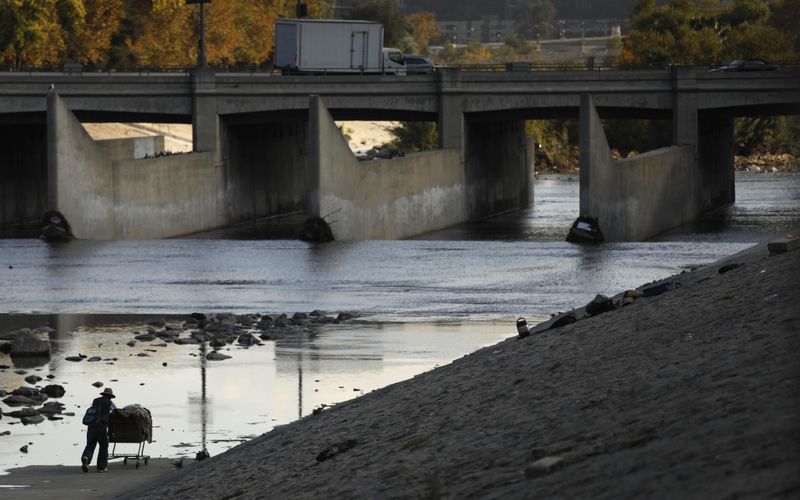 A man carts his belongings along the L.A. River to higher ground before a rainstorm flooded his camp on an island in the middle of the L.A. River near Atwater Village in November 2018. (Genaro Molina / Los Angeles Times)