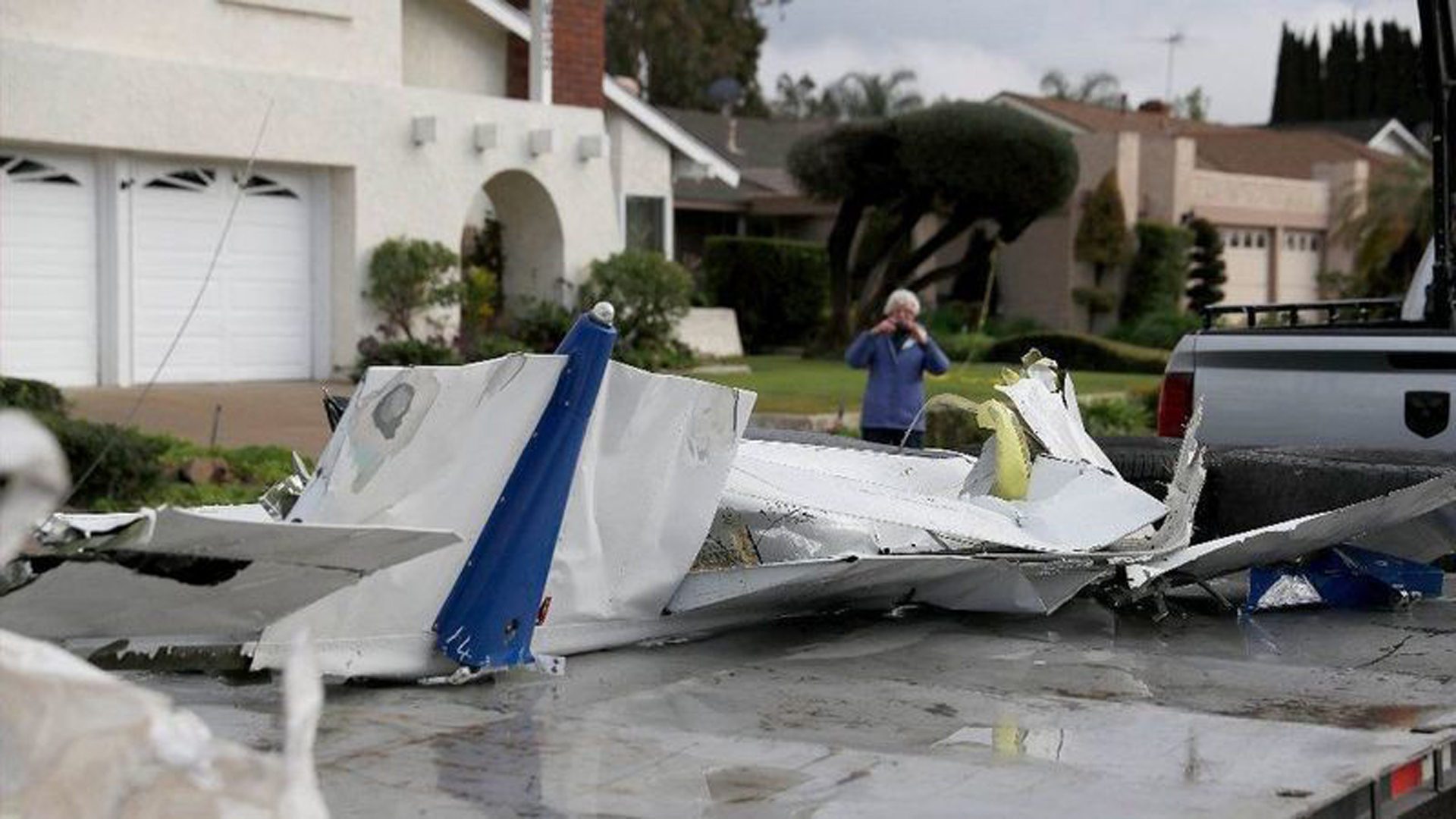 A woman takes a photo of airplane parts that landed on her property as workers remove wreckage after the crash of a Cessna airplane in Yorba Linda on Sunday, killing the pilot and four people inside a home. (Credit: Allen J. Schaben / Los Angeles Times)