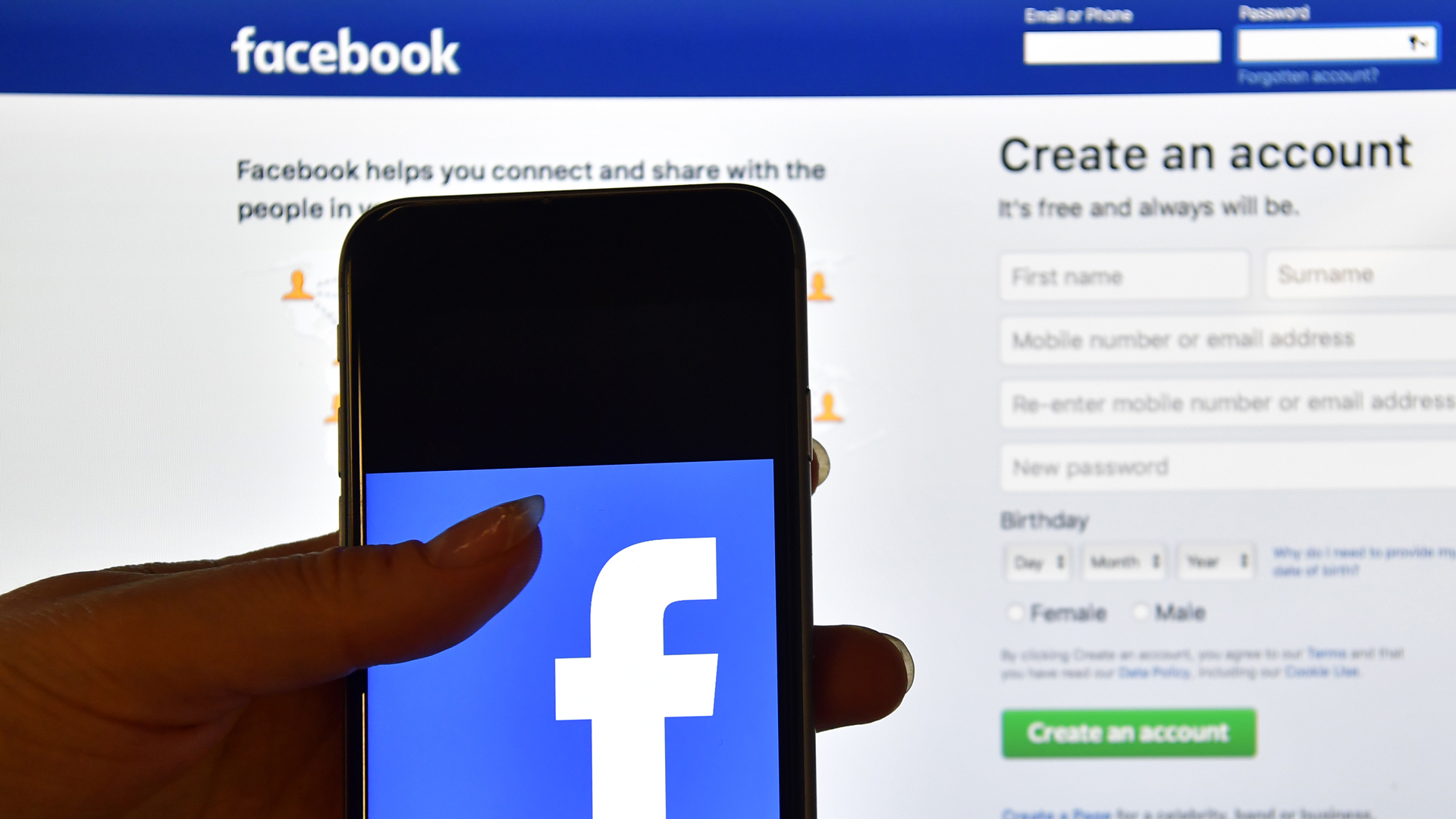 A person holds an iPhone displaying the Facebook app logo in front of a computer screen showing the Facebook login page on August 3, 2016 in London, England. (Credit: Carl Court/Getty Images)