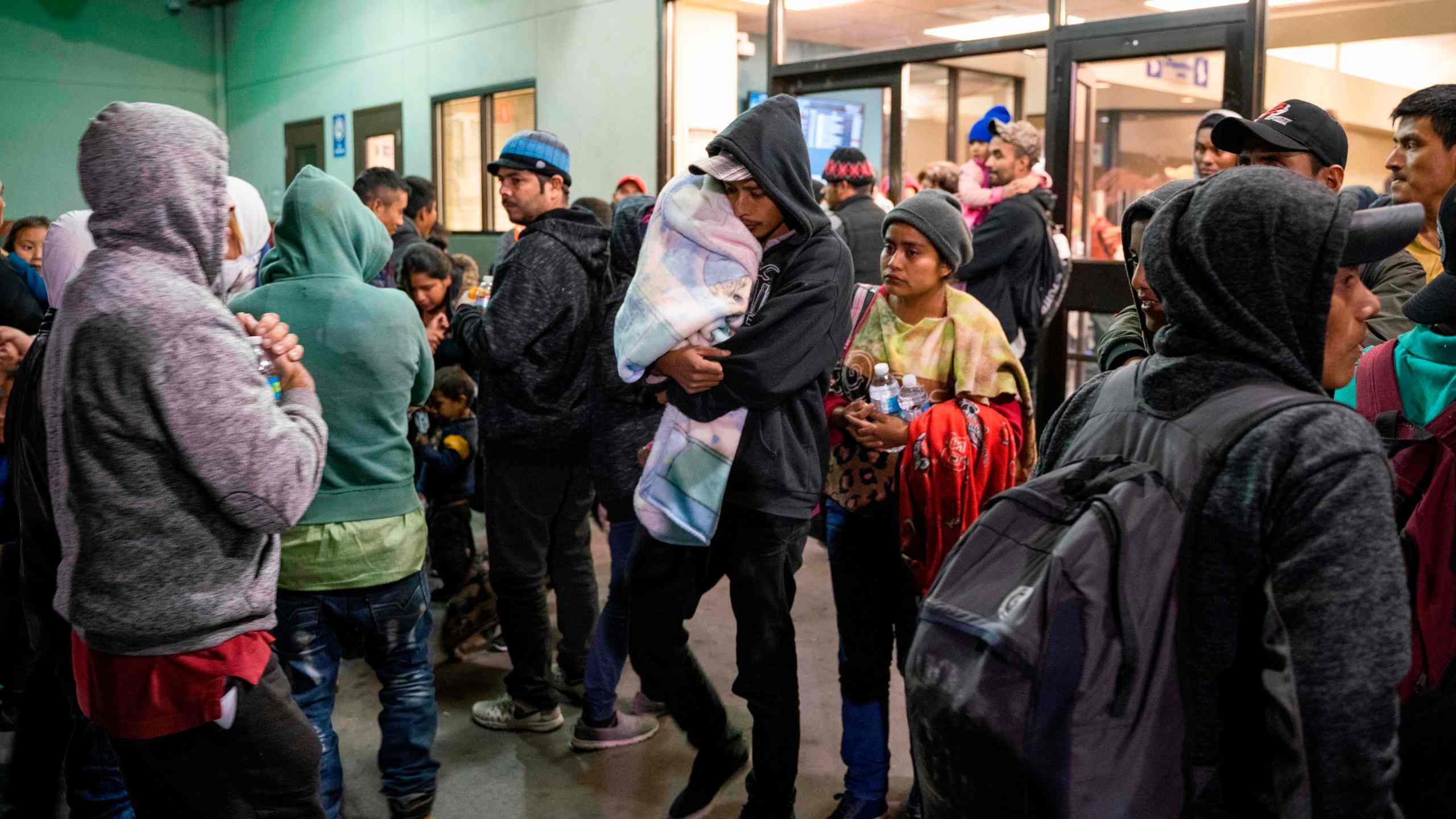 Asylum seekers stand at a bus stop after being dropped off by Immigration and Customs Enforcement at the Greyhound bus station in downtown El Paso, Texas late on Dec. 23, 2018. (Credit: PAUL RATJE/AFP/Getty Images)