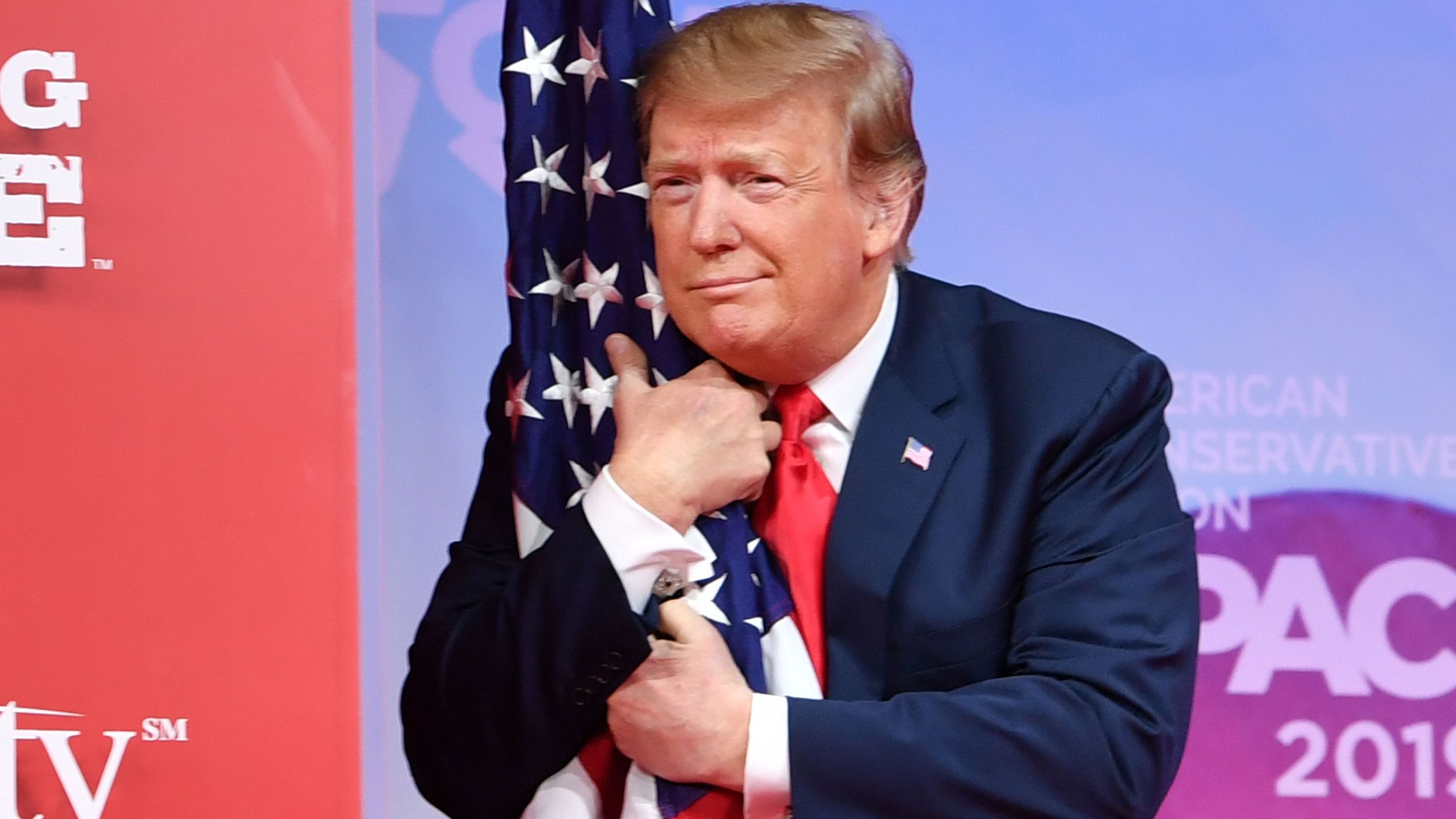 Donald Trump hugs the U.S. flag as he arrives to speak at the annual Conservative Political Action Conference in National Harbor, Maryland, on March 2, 2019. (Credit: NICHOLAS KAMM/AFP/Getty Images)