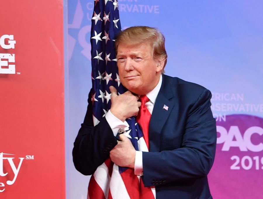 Donald Trump hugs the U.S. flag as he arrives to speak at the annual Conservative Political Action Conference in National Harbor, Maryland, on March 2, 2019. (Credit: NICHOLAS KAMM/AFP/Getty Images)