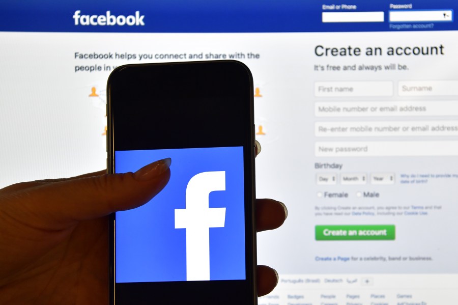 A person holds an iPhone displaying the Facebook app logo in front of a computer screen showing the Facebook login page on August 3, 2016 in London, England. (Credit: Carl Court/Getty Images)