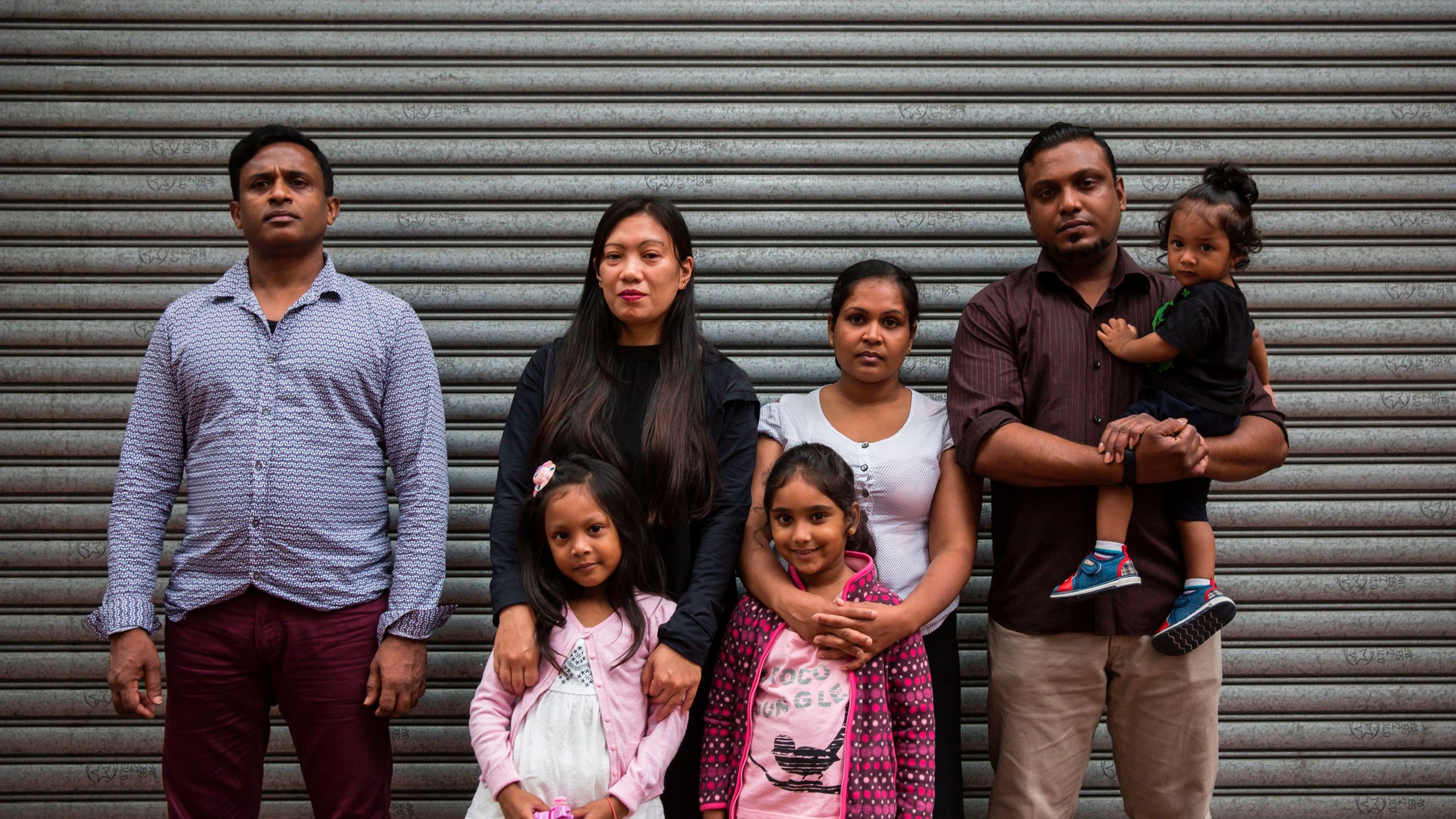 Sri Lankan refugee Ajith Puspa (left), Filipino refugee Vanessa Rodel (second from left) with her daughter Keana, Sri Lankan refugees Nadeeka Nonis (third from right) with her partner Supun Thilina Kellapatha (second from right) and children Sethumdi (fourth from right) and Dinath (right) pose for a photo in front of the Torture Claims Appeal Board building in Hong Kong on July 17, 2017, before attending an appeal hearing over the rejection of their refugee status in the southern Chinese city. (Credit: ISAAC LAWRENCE/AFP/Getty Images)