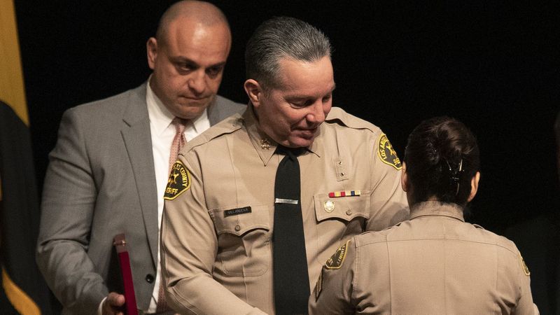 Los Angeles County Sheriff's Deputy Caren Mandoyan, left, looks on as newly elected L.A. Sheriff Alex Villanueva prepares to have his new badge pinned on him by his wife during a ceremony Dec. 3, 2018. (Credit: Mel Melcon / Los Angeles Times)