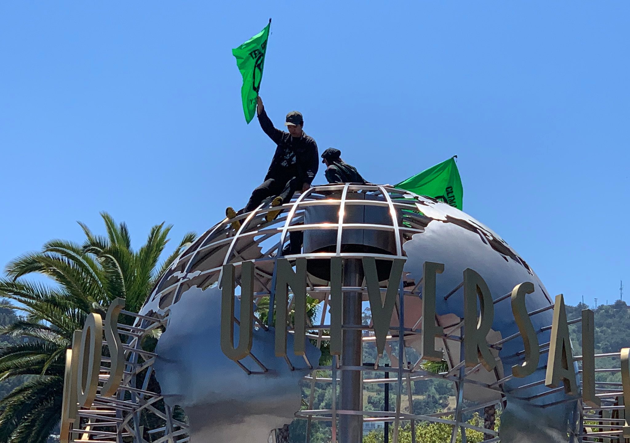 Two protesters sit atop the globe at Universal Studios Hollywood on April 22, 2019. (Credit: @Secretkat3 via Twitter)